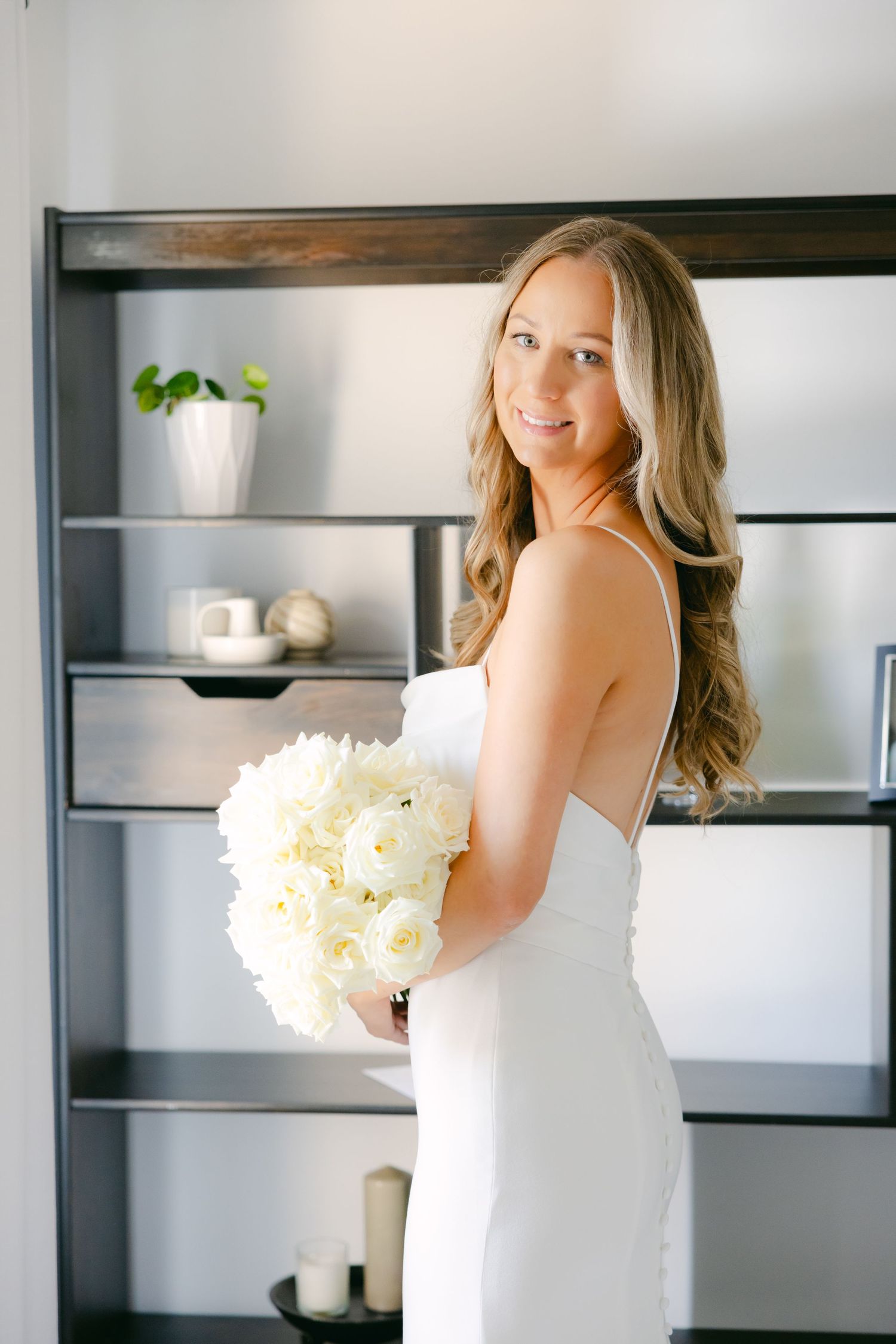 White wedding dress and bouquet photographed against modern built-in shelving.
