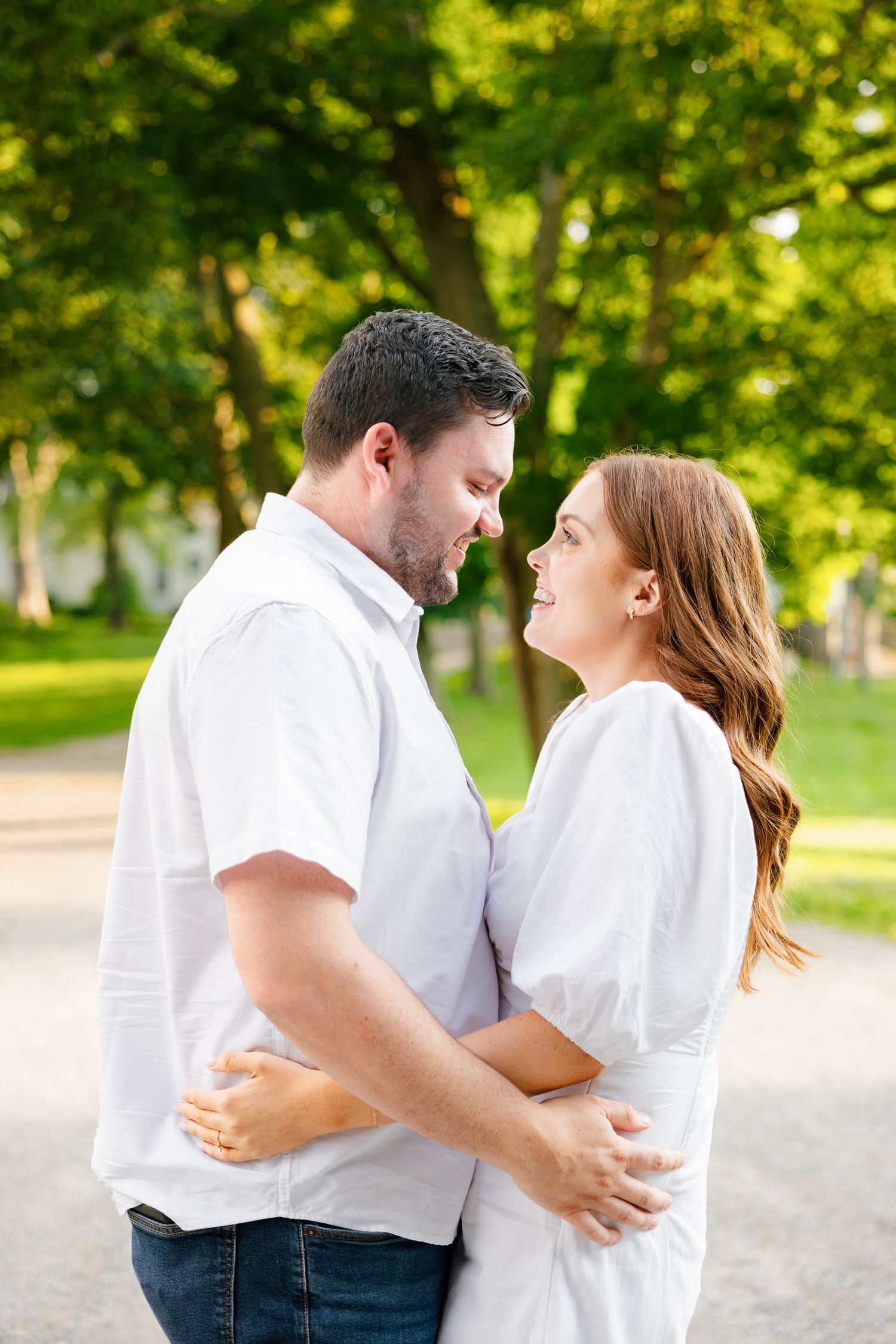 A couple sharing an intimate moment while embracing in a leafy park setting.