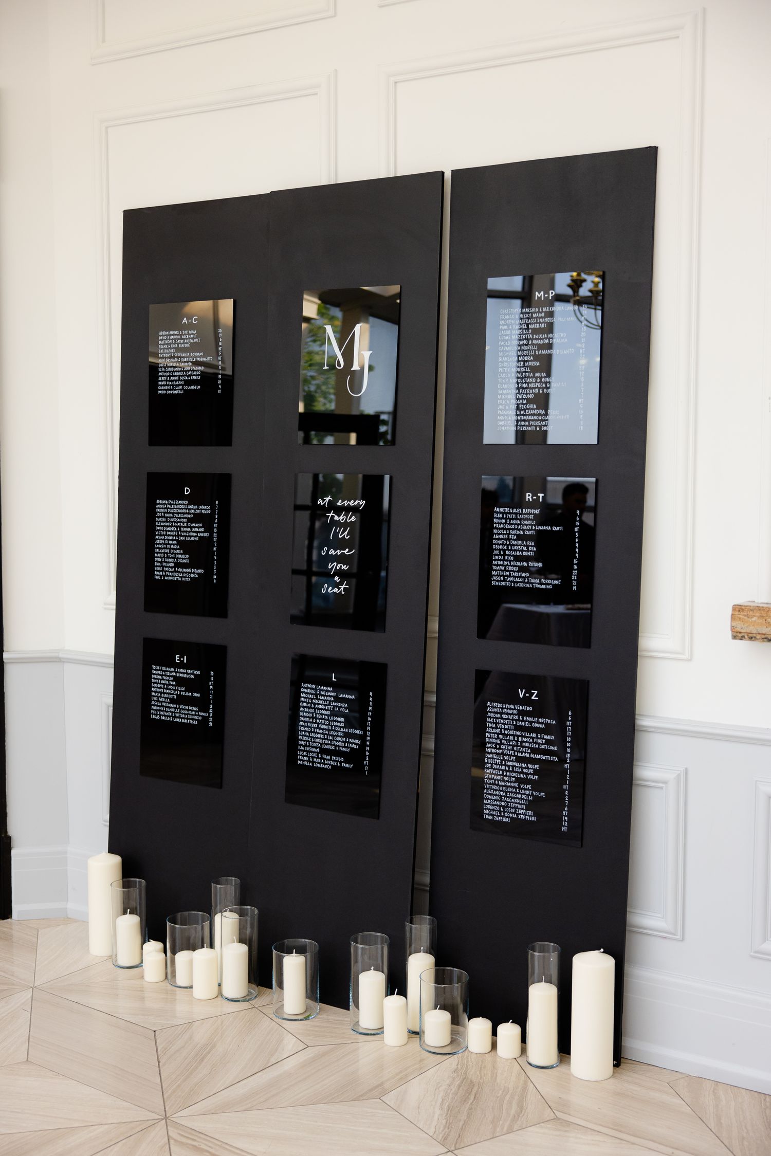 Modern black seating chart display with white text and candles at the base for wedding reception.