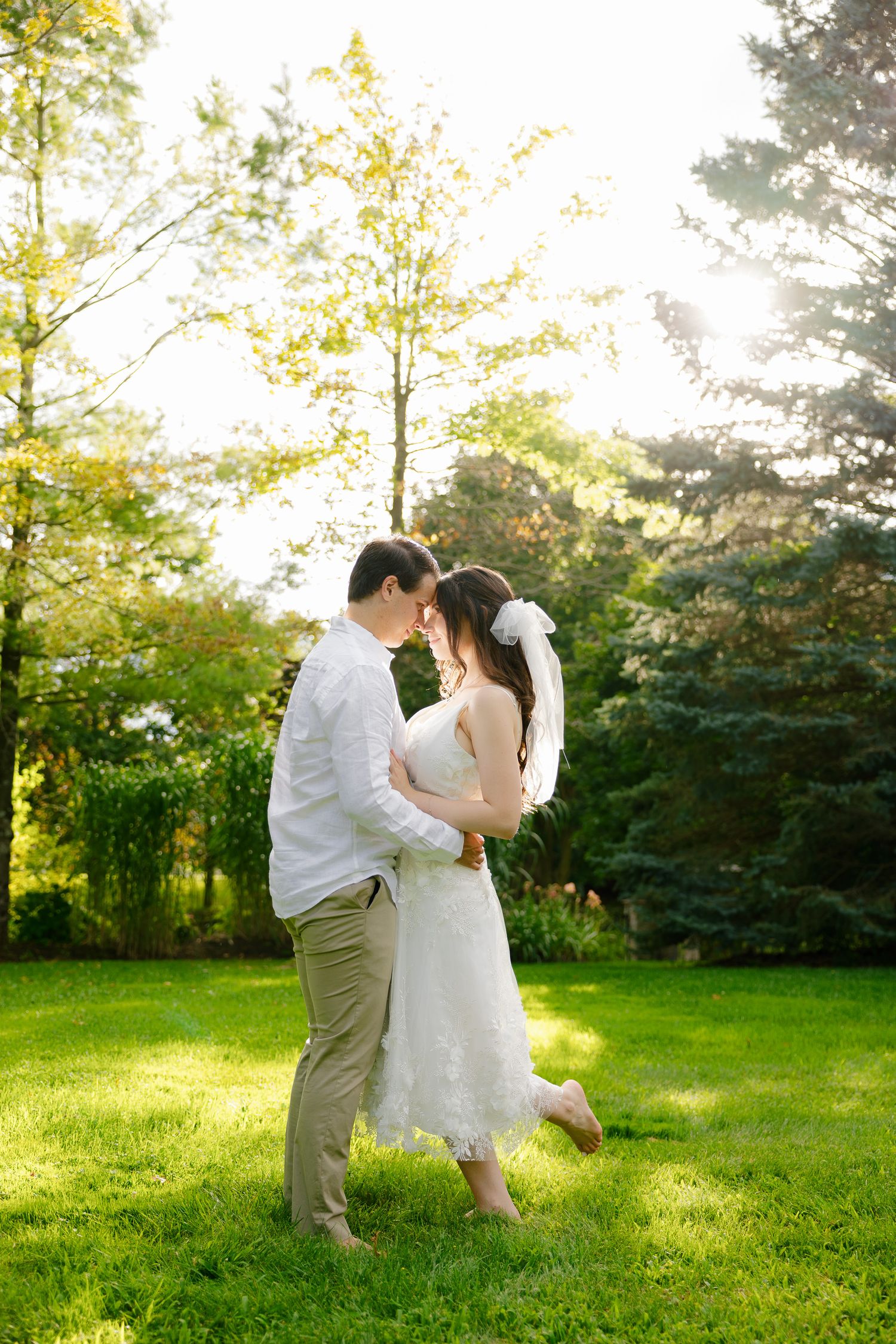 Sun-drenched garden wedding portrait with couple sharing an intimate moment among trees.