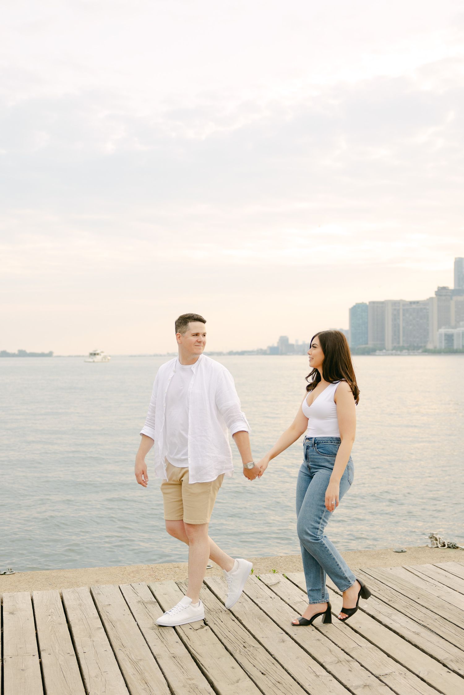 Couple strolling together on wooden pier with Toronto harbor skyline in background.