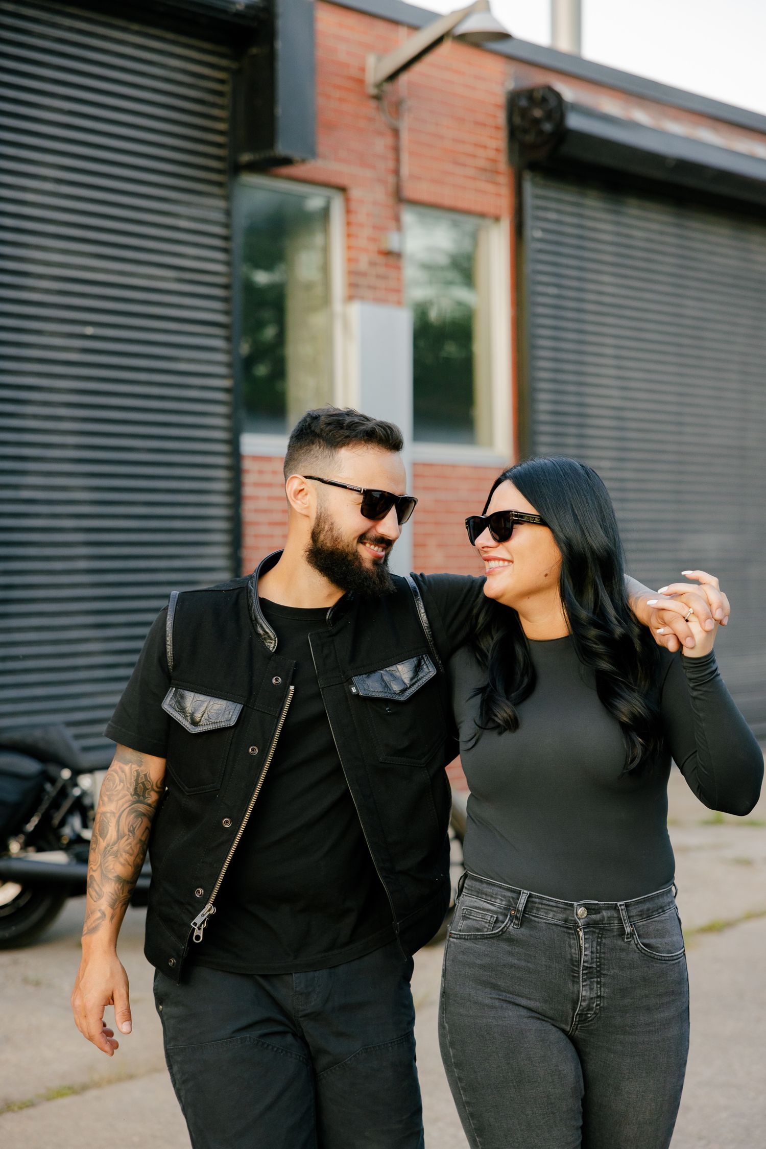 A couple sharing a joyful moment while walking outdoors in matching dark attire.