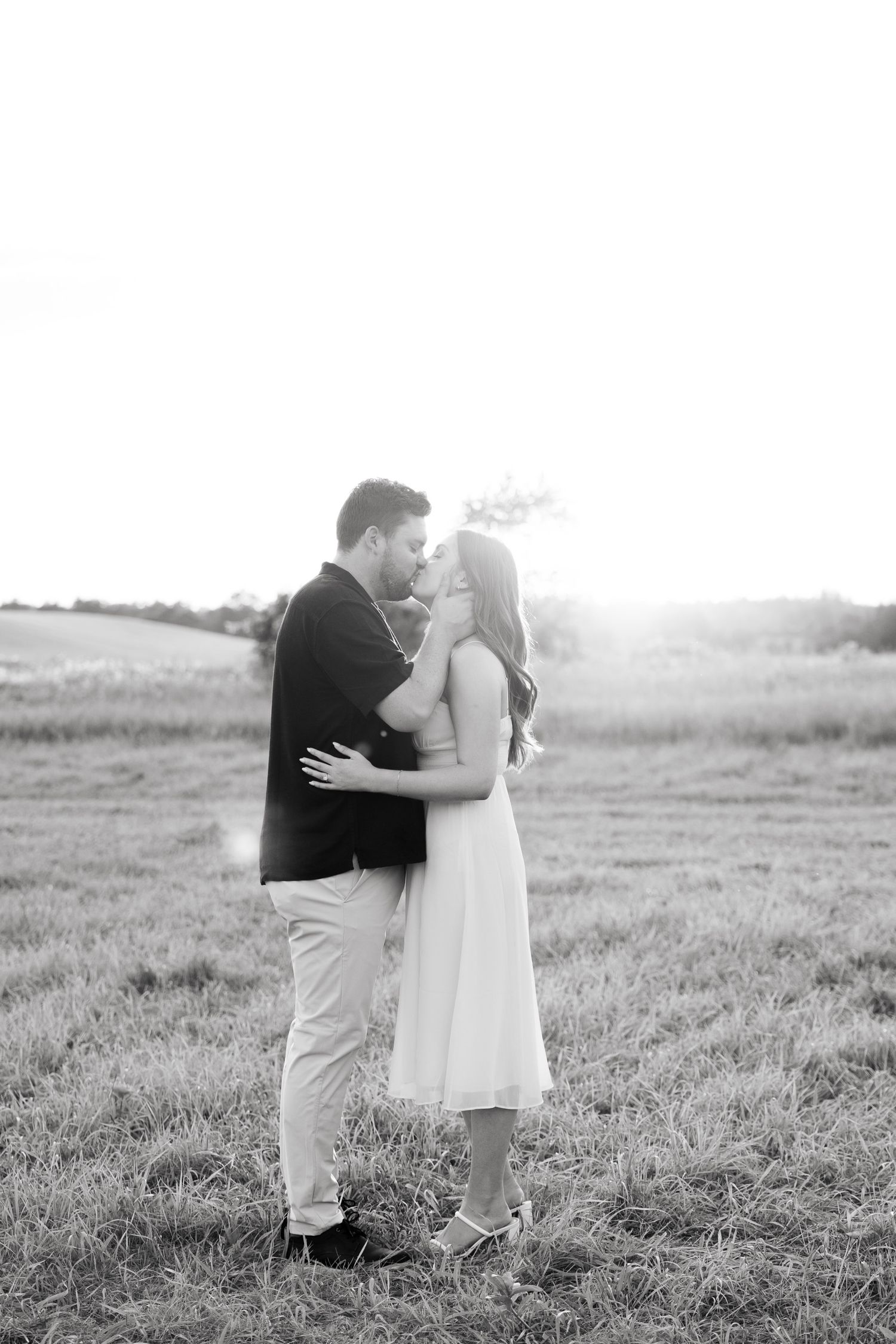 Romantic black and white portrait of a couple embracing in a sunlit meadow at golden hour.