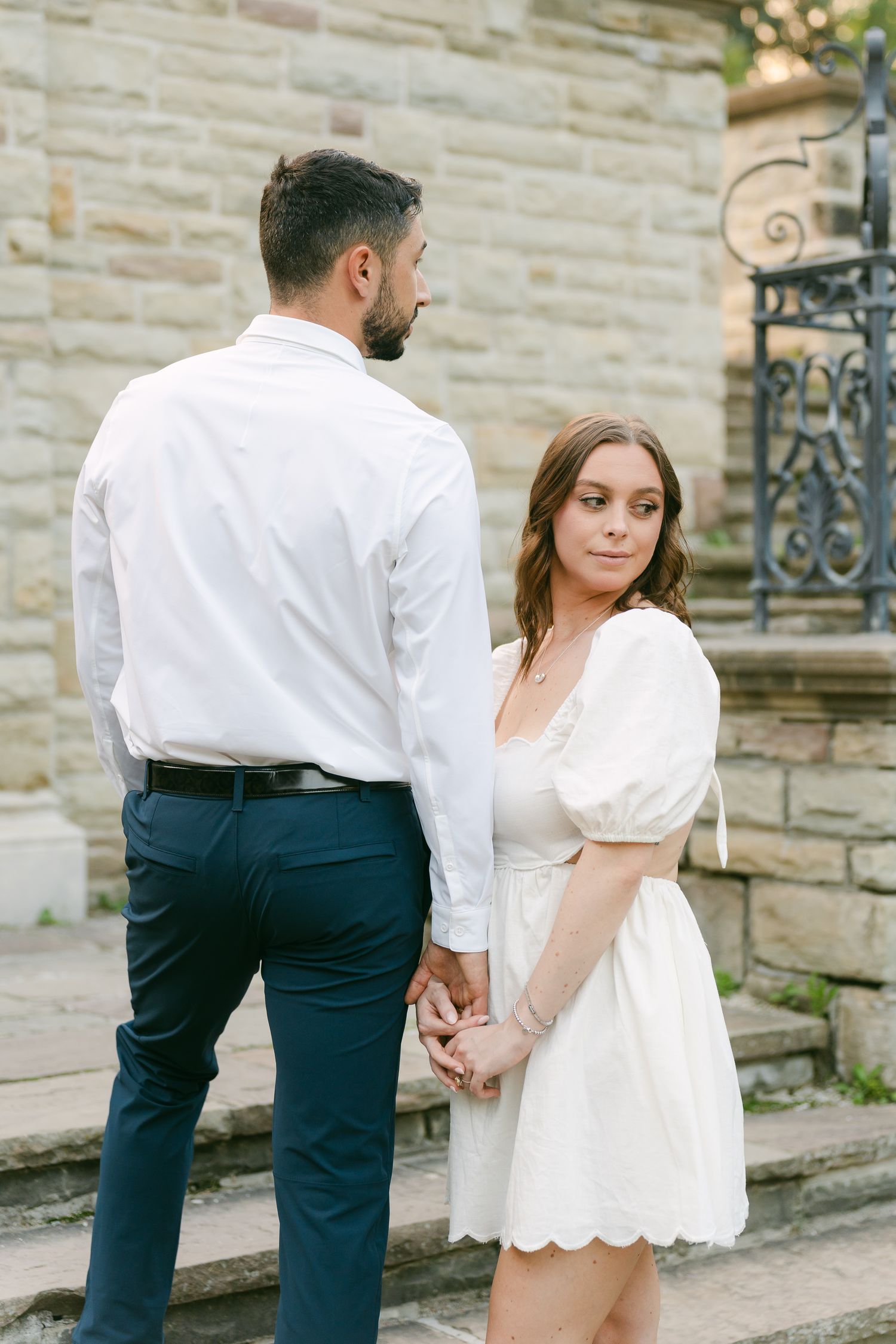 A couple in white and navy outfits holding hands on stone steps with a classic architectural backdrop.