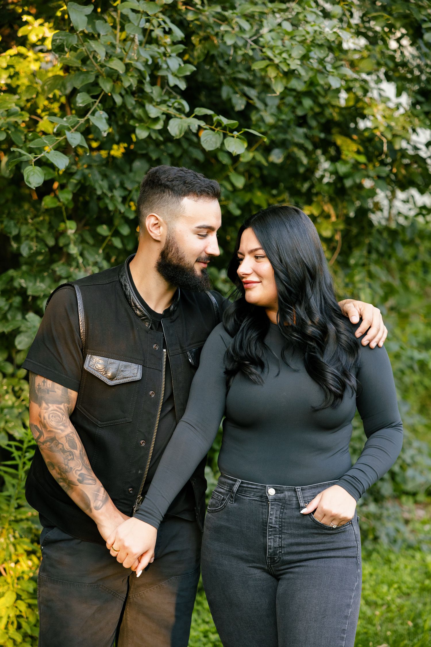 A couple shares an intimate moment together outdoors against a backdrop of green foliage.