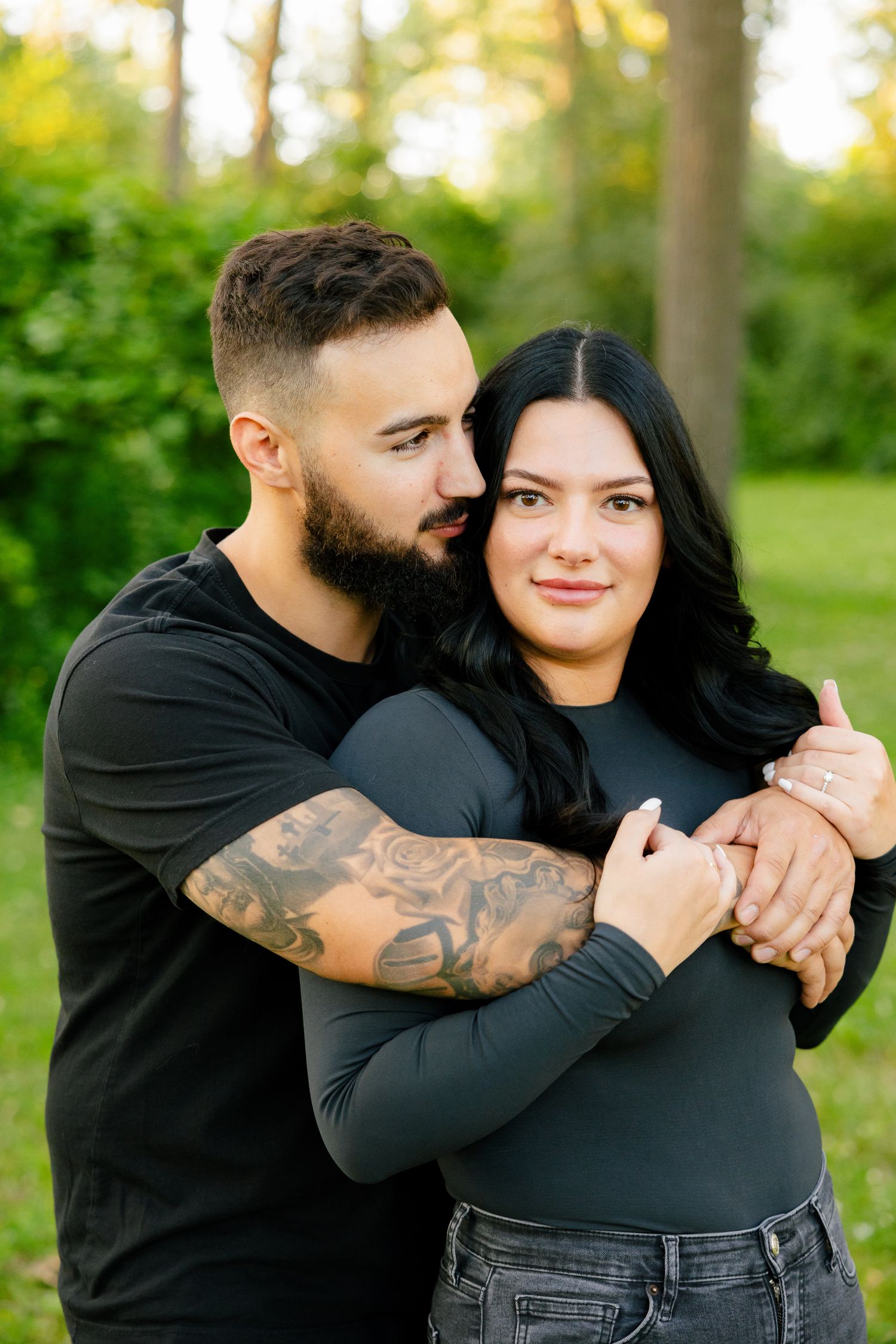 Couple in matching black tops share loving embrace amid lush green outdoor setting.