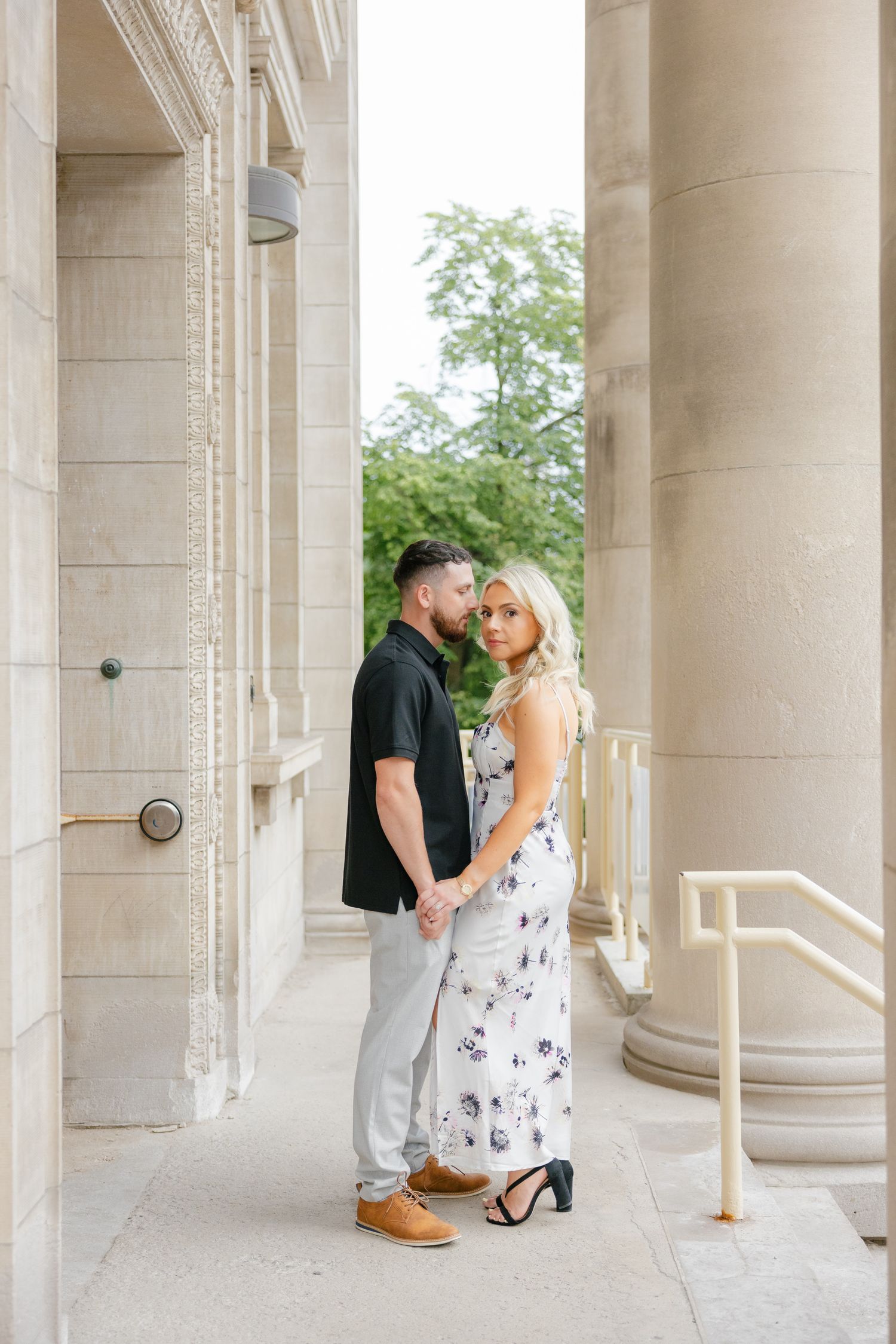 Couple shares an intimate moment between tall stone pillars while dressed in contrasting black and floral outfits.