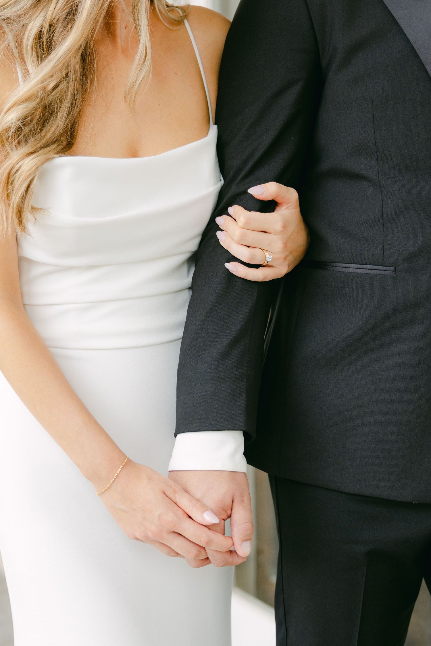 Detail shot of couple's hands and formal wedding attire in black and white.