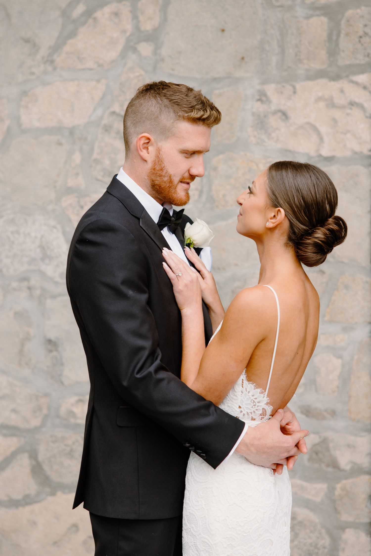 A romantic wedding moment as a couple embraces in formal attire against a stone wall backdrop.