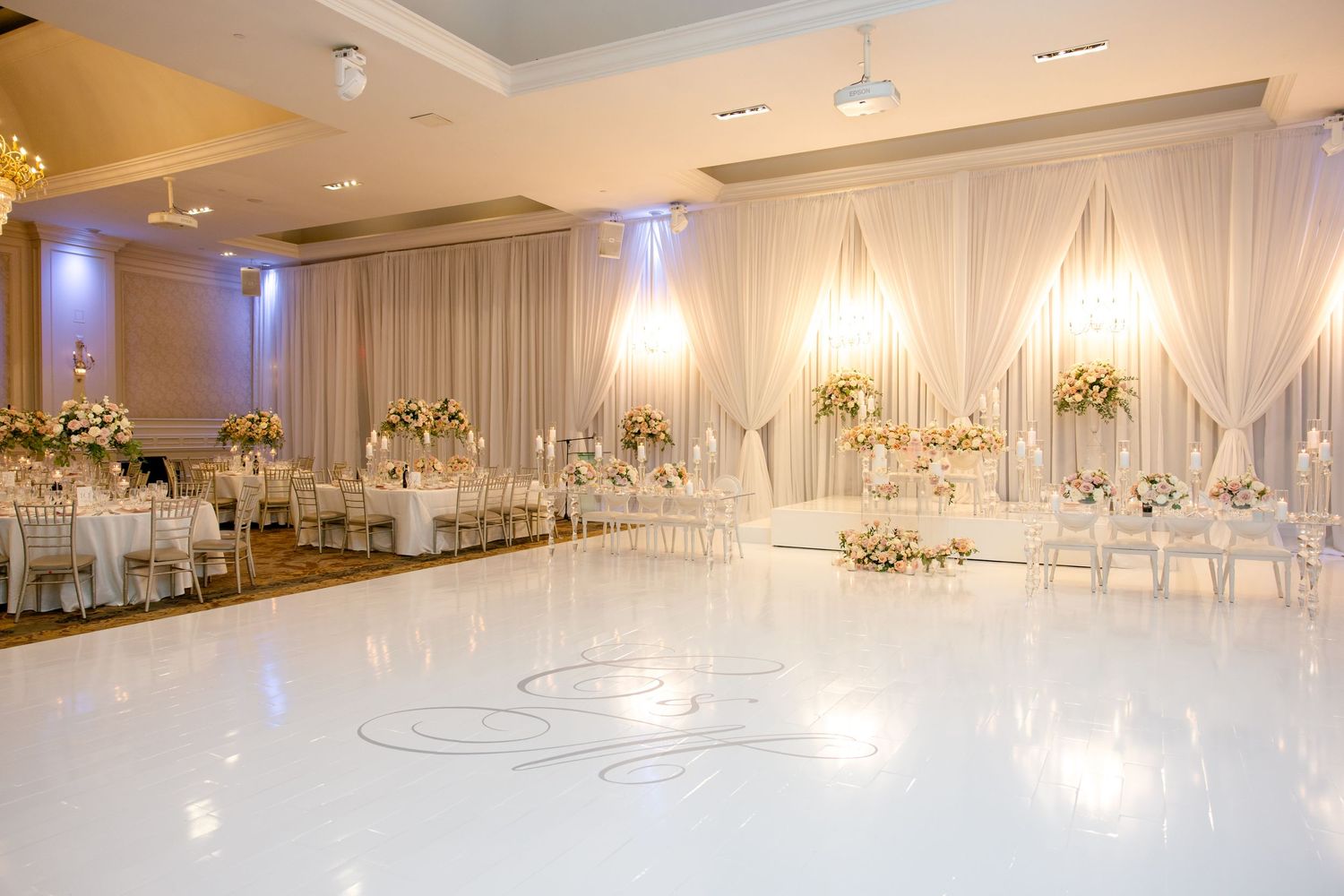 Spacious wedding reception venue with white draping, crystal lighting and glossy white dance floor.