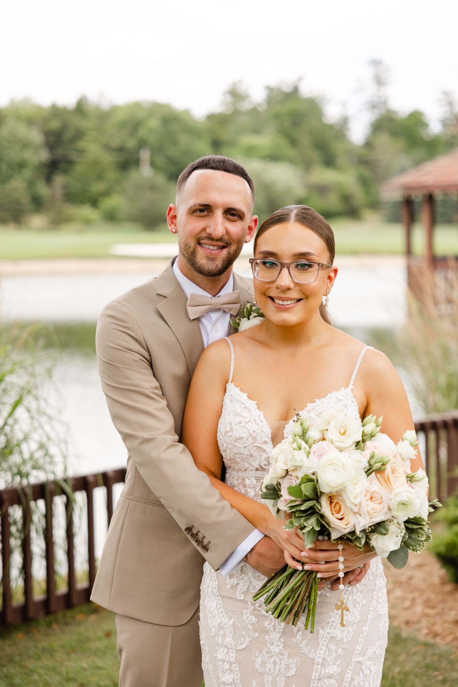 Wedding portrait showing couple on wooden deck with lake and garden scenery in background.