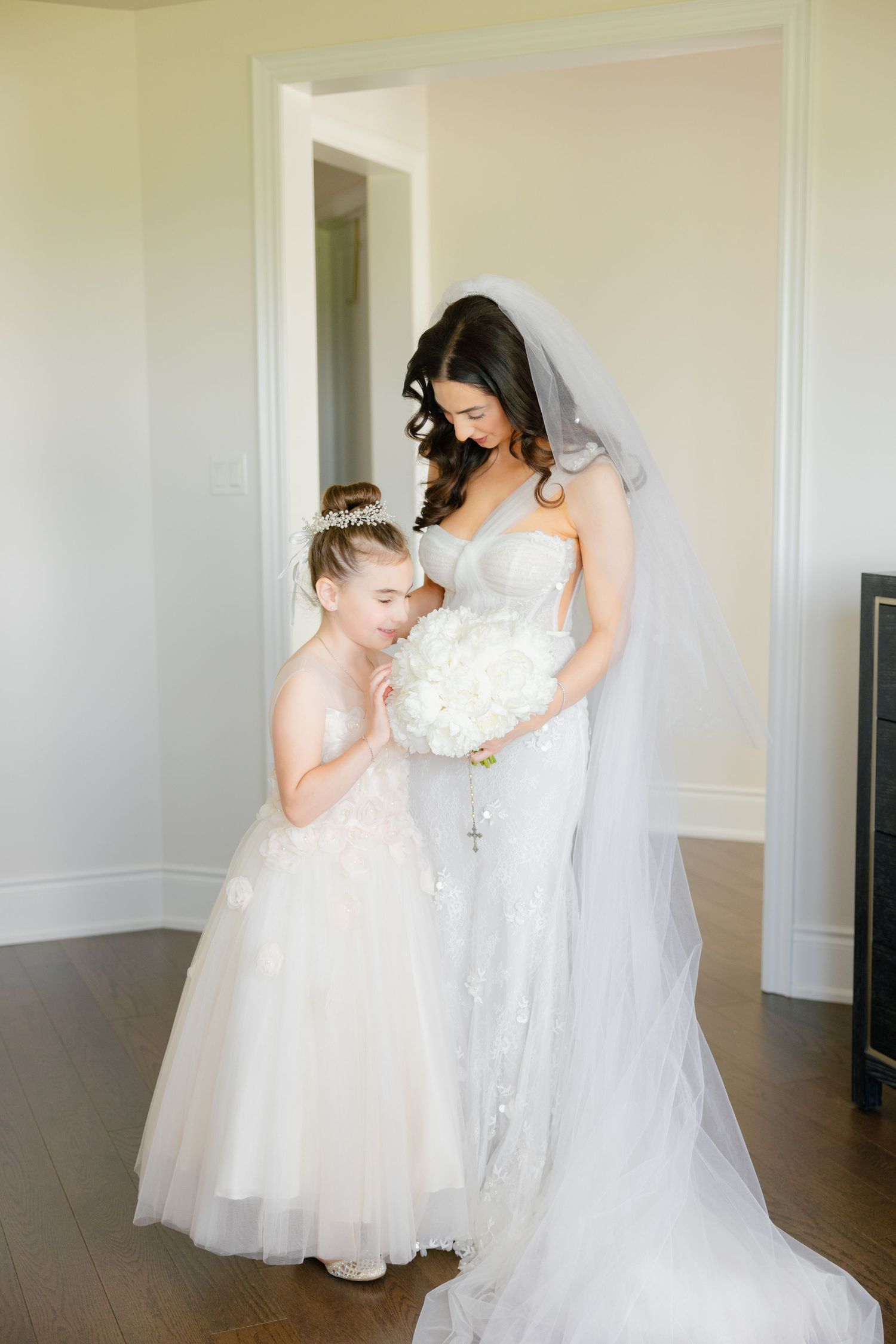 A tender moment between a bride in white and a young flower girl in a matching dress.