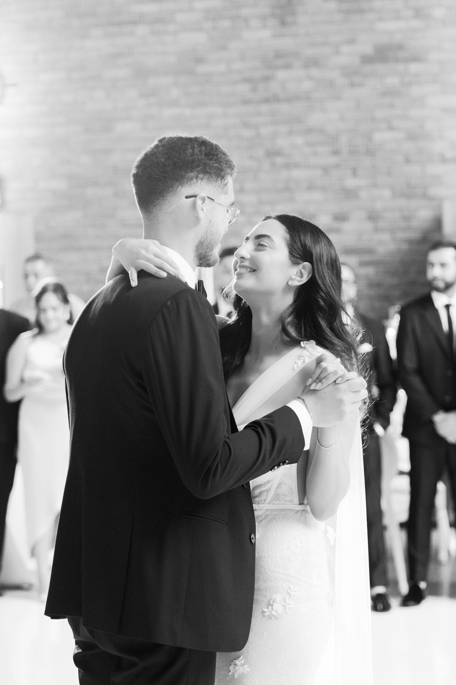 Intimate wedding dance moment captured in black and white against brick wall backdrop.