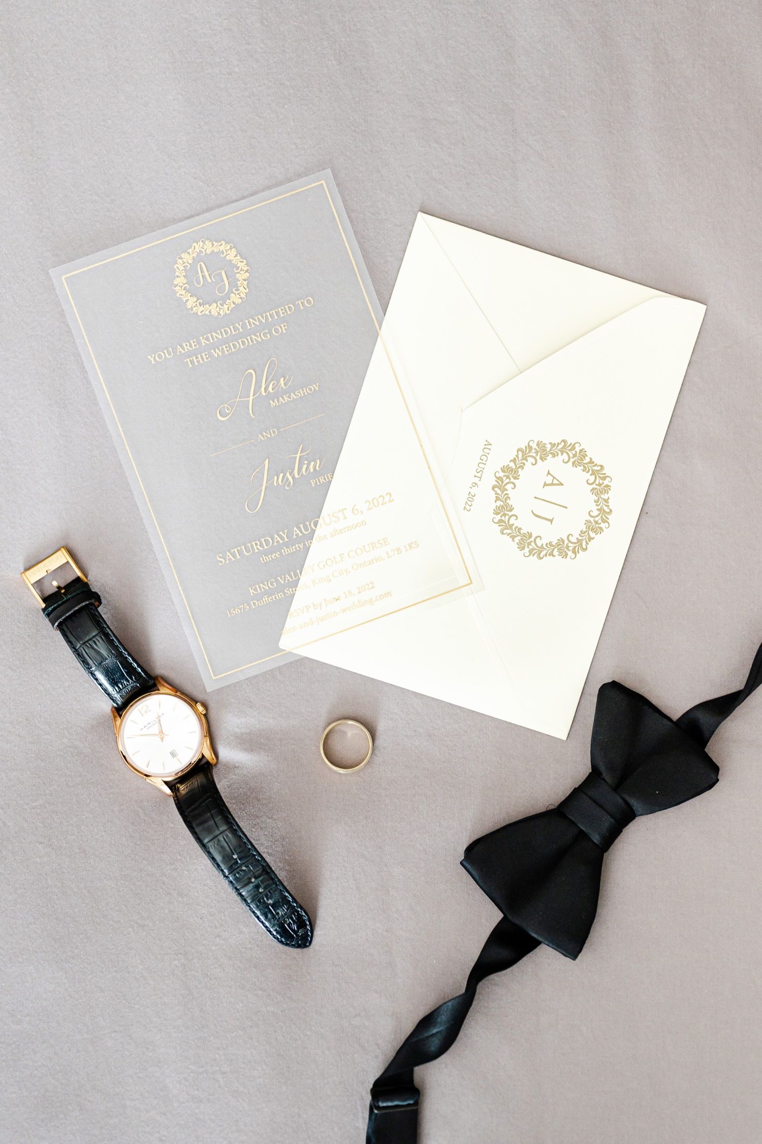 Elegant wedding stationery with gold monogram, watch and black bow tie on gray background.