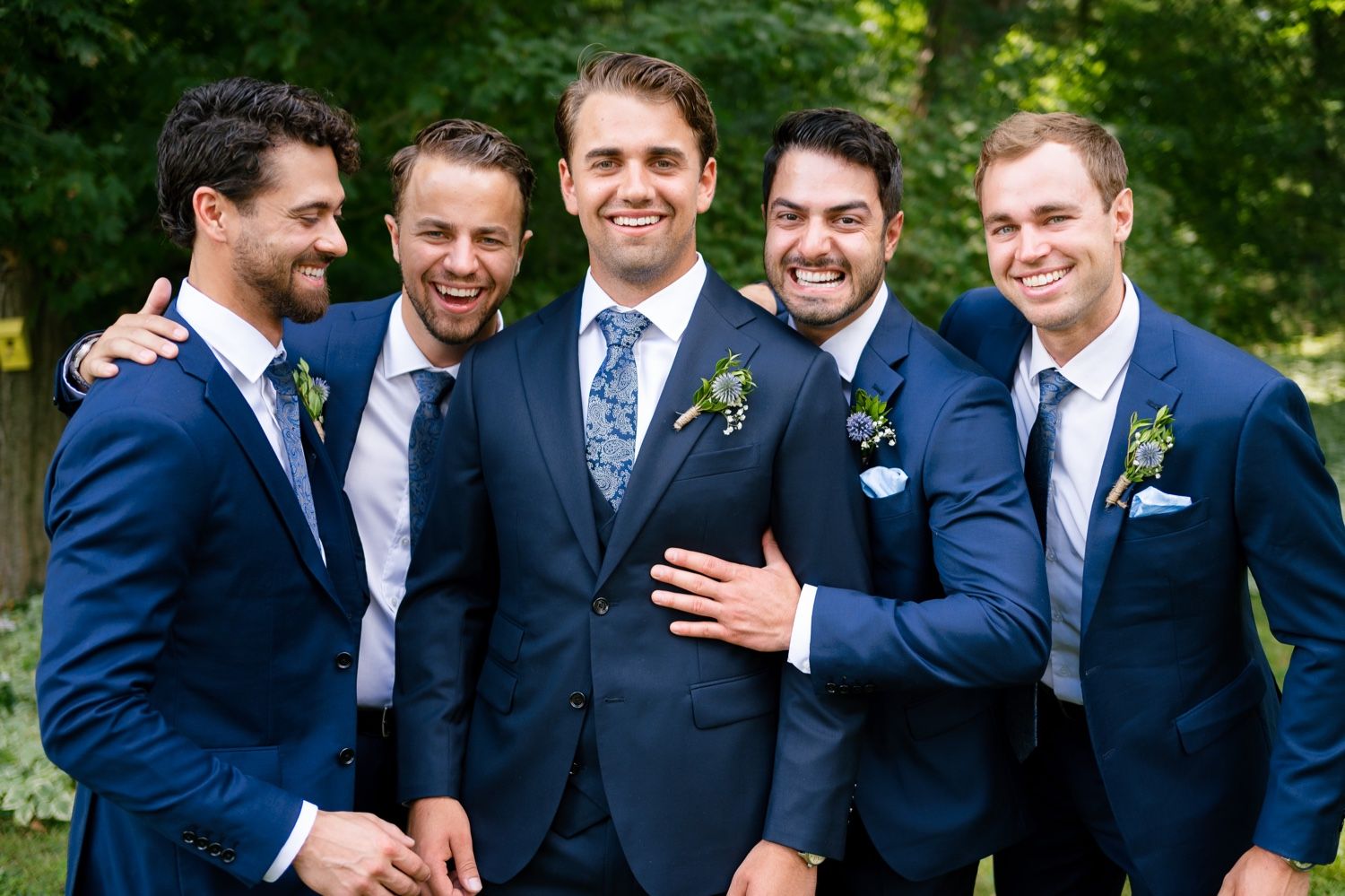 Groomsmen share a candid moment while posing in navy and grey suits with boutonnieres.