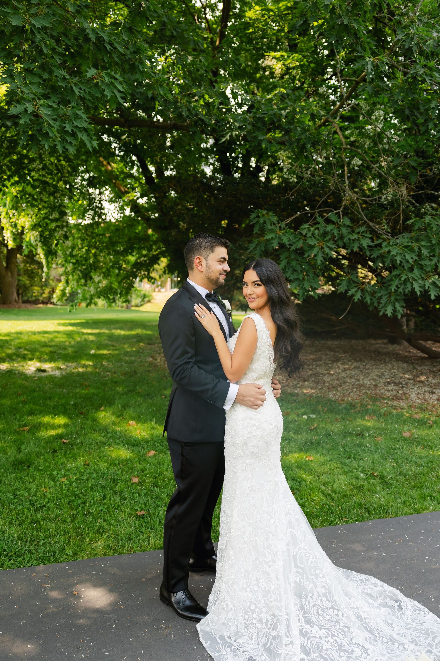A stunning wedding portrait of a couple posed against lush greenery with a trailing lace gown.
