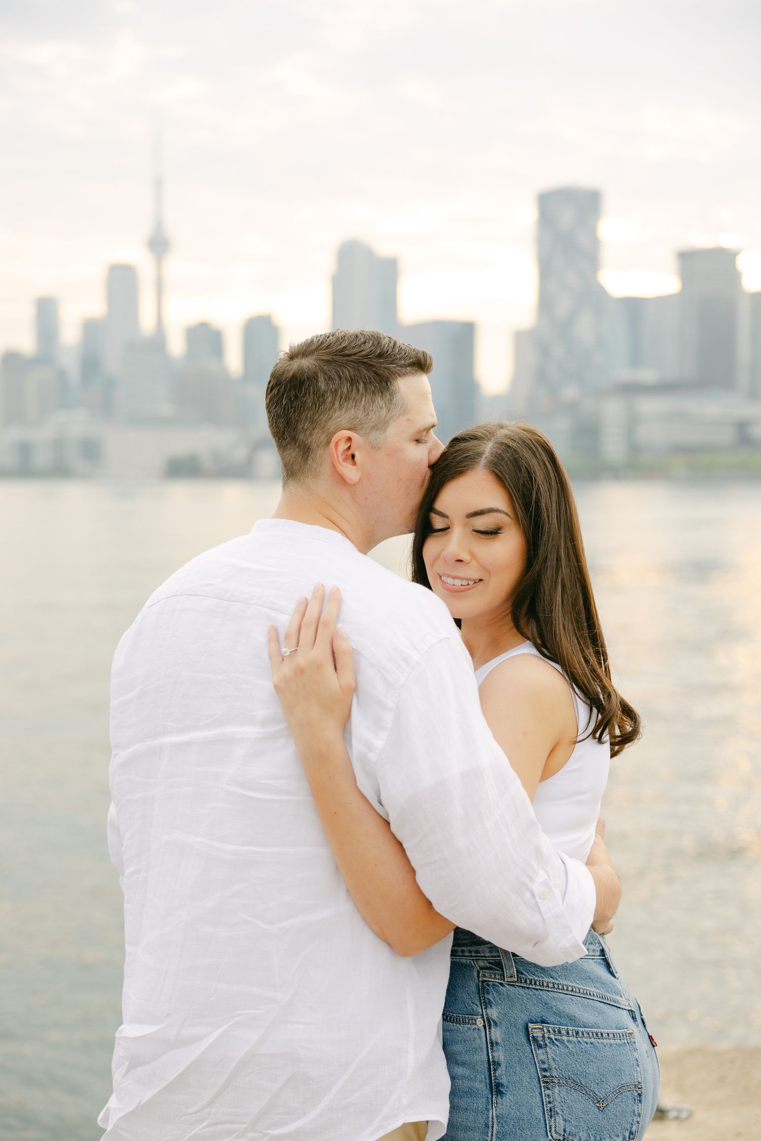 A loving embrace captured against Toronto's waterfront with soft lighting and urban architecture.