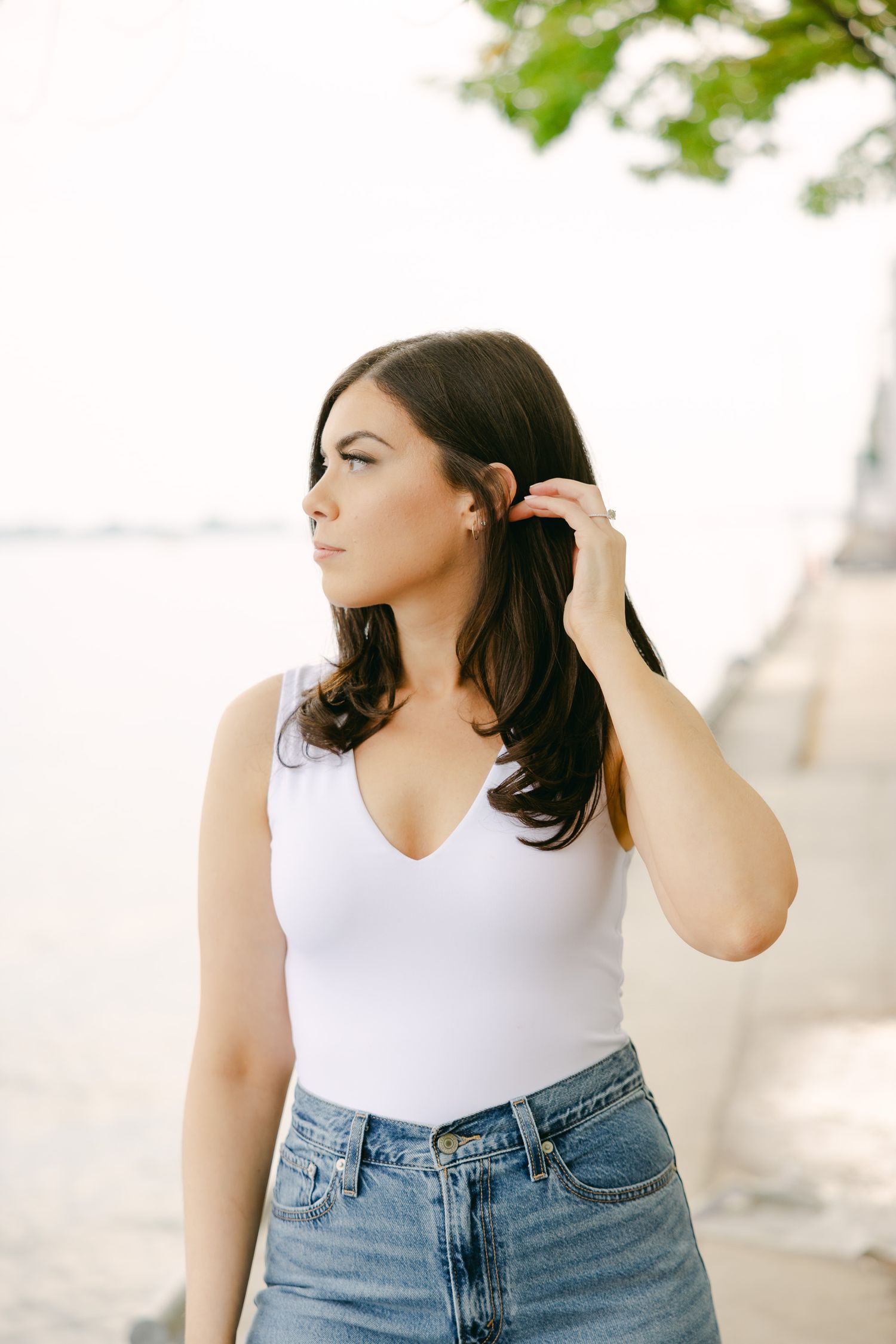 Person in casual summer outfit adjusts hair while posing by waterfront.
