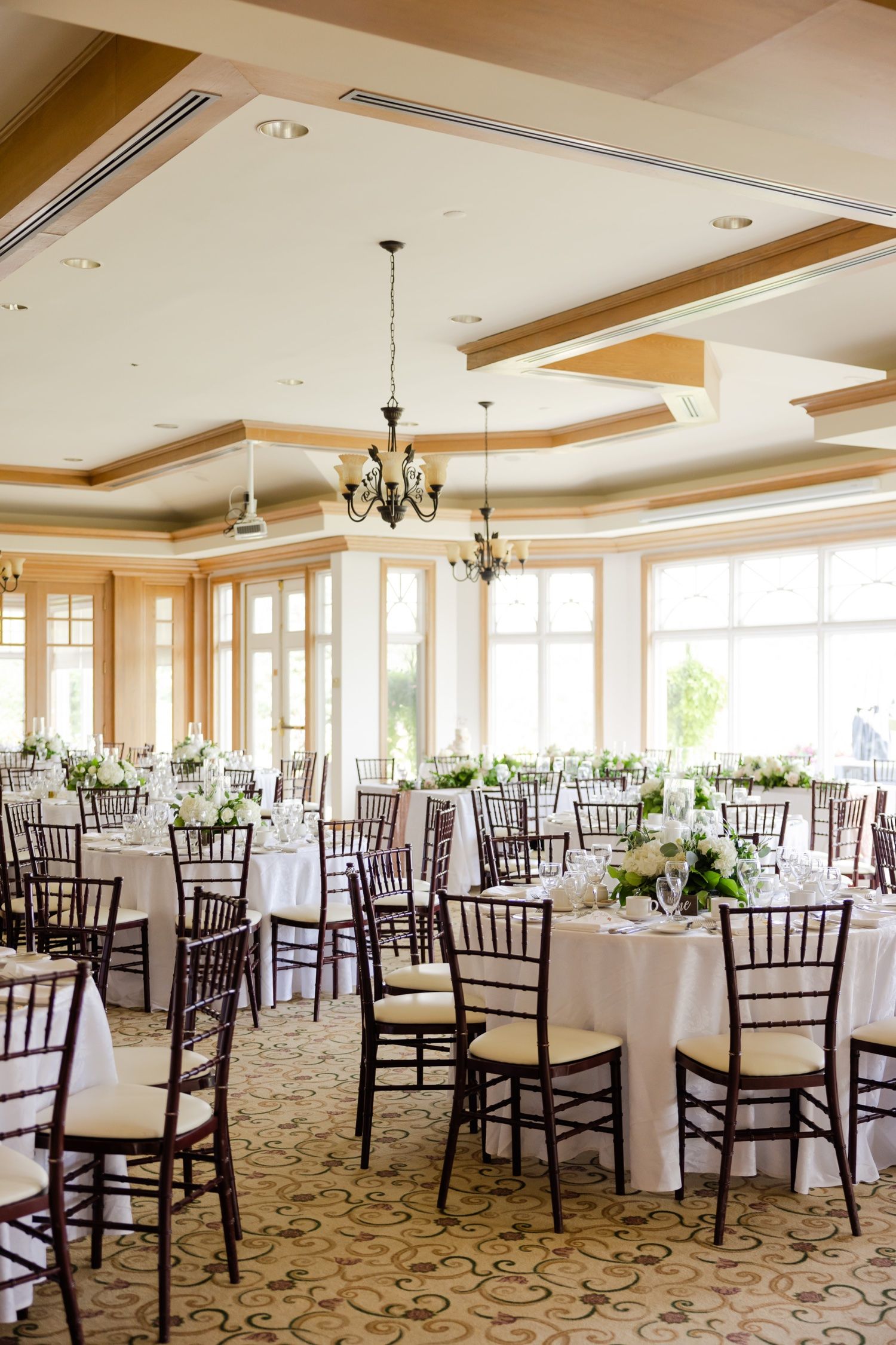 Bright ballroom setup with round tables, chiavari chairs, and crystal chandeliers for an elegant wedding reception.
