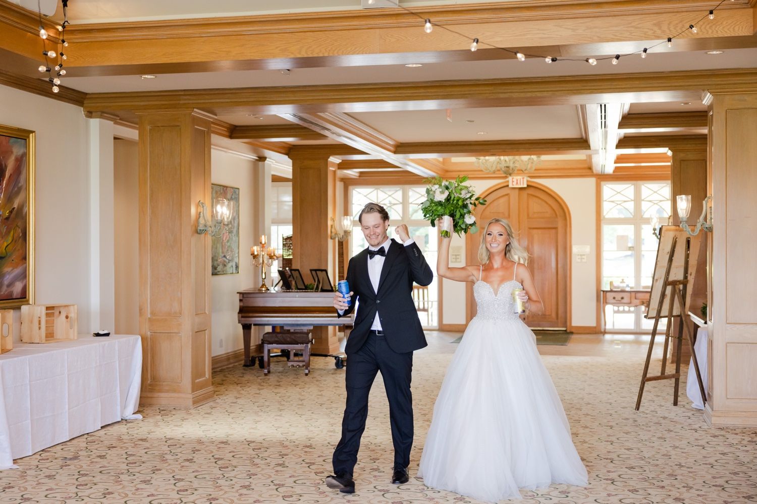 Couple dancing joyfully in an elegant ballroom with exposed wooden beams and string lights.