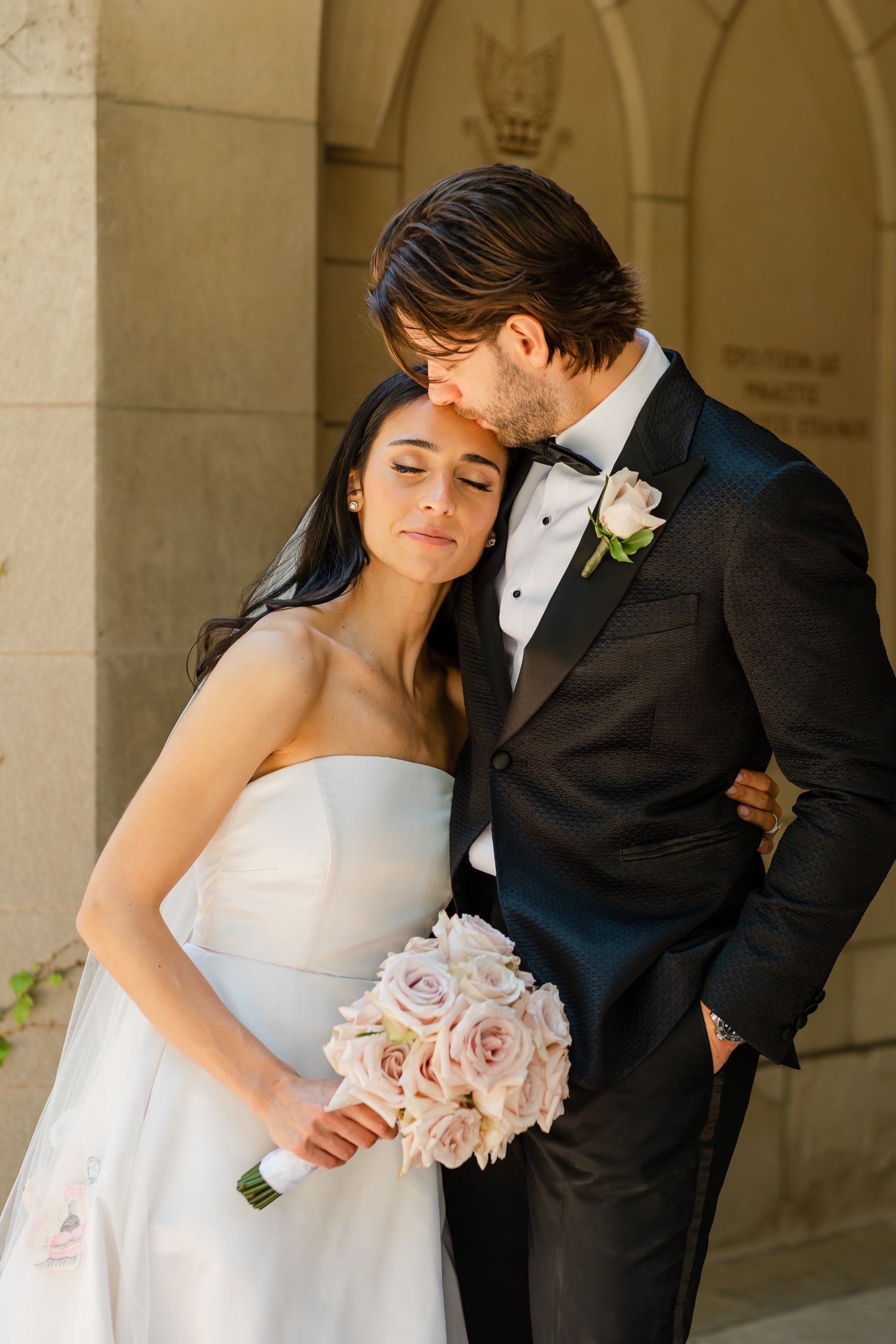 Intimate wedding moment with pink bouquet under ornate stone archway.