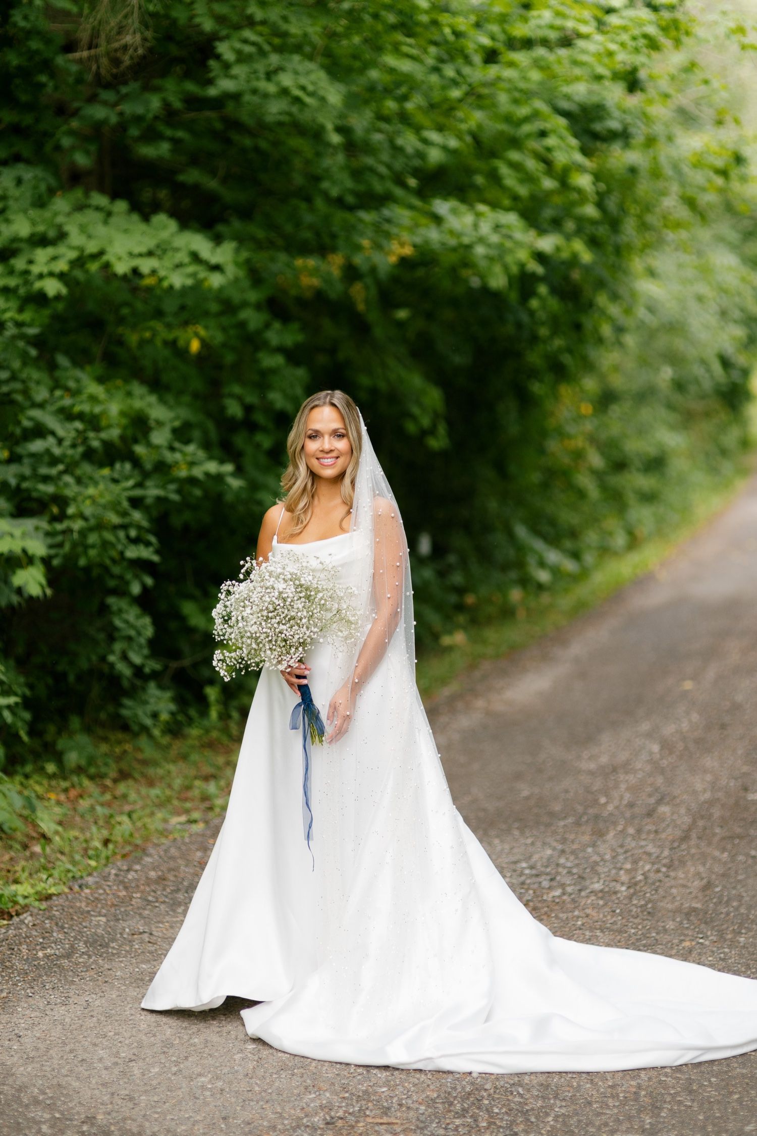 Full length bridal portrait on wooded path with flowing train and baby's breath bouquet.