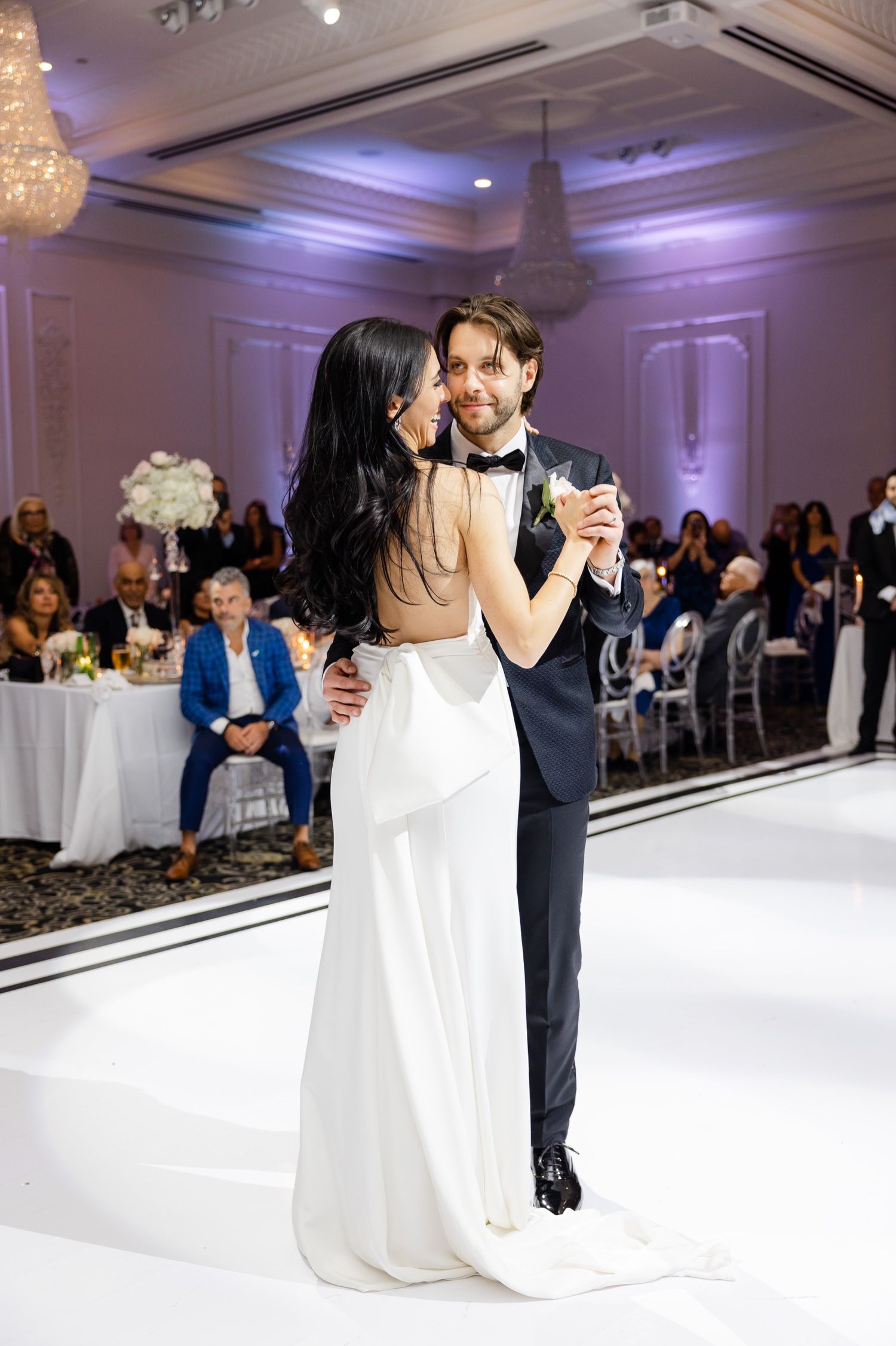 Elegant first dance moment captured in purple-lit ballroom with crystal chandeliers.