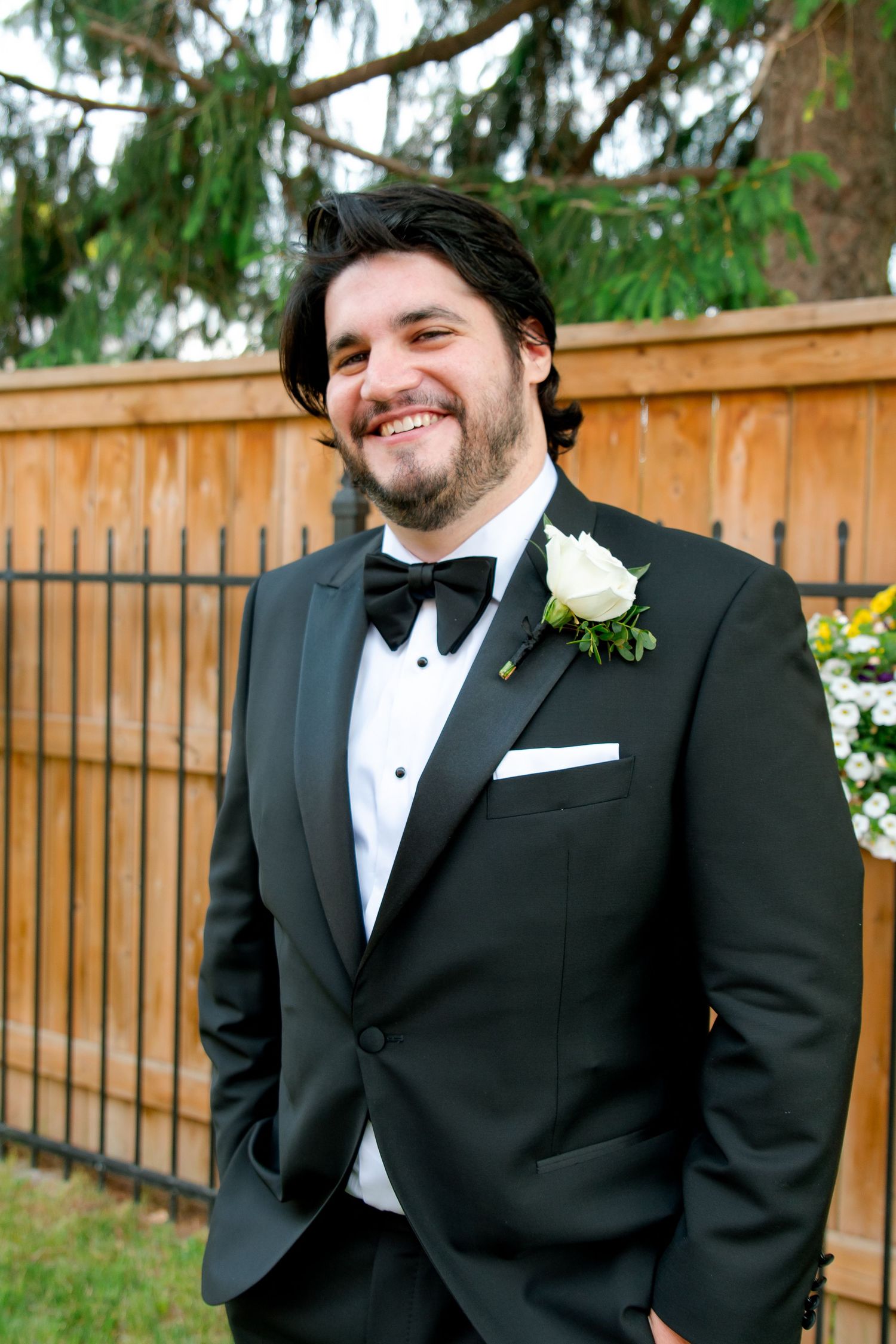Formal attire with black bow tie and white boutonniere against wooden fence backdrop.