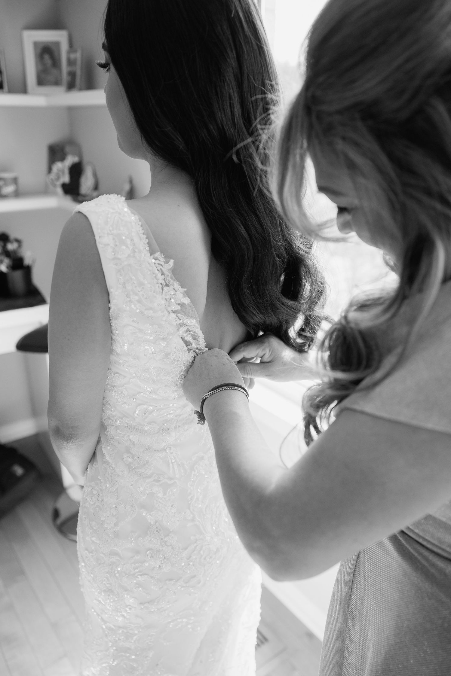 Black and white photo showing delicate lace details being fastened on a wedding dress.