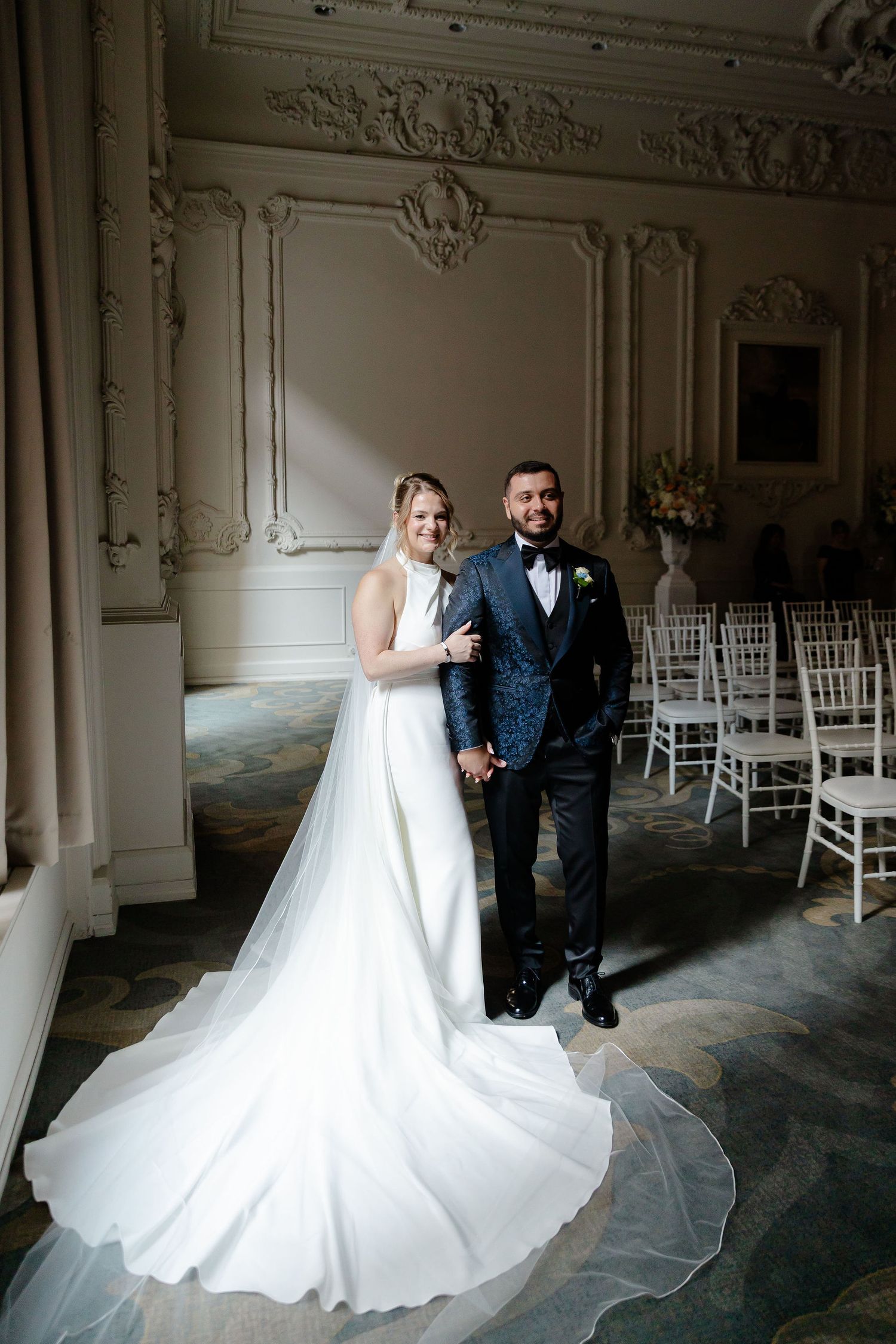 Elegant wedding couple photographed in ornate white ballroom with decorative moldings.