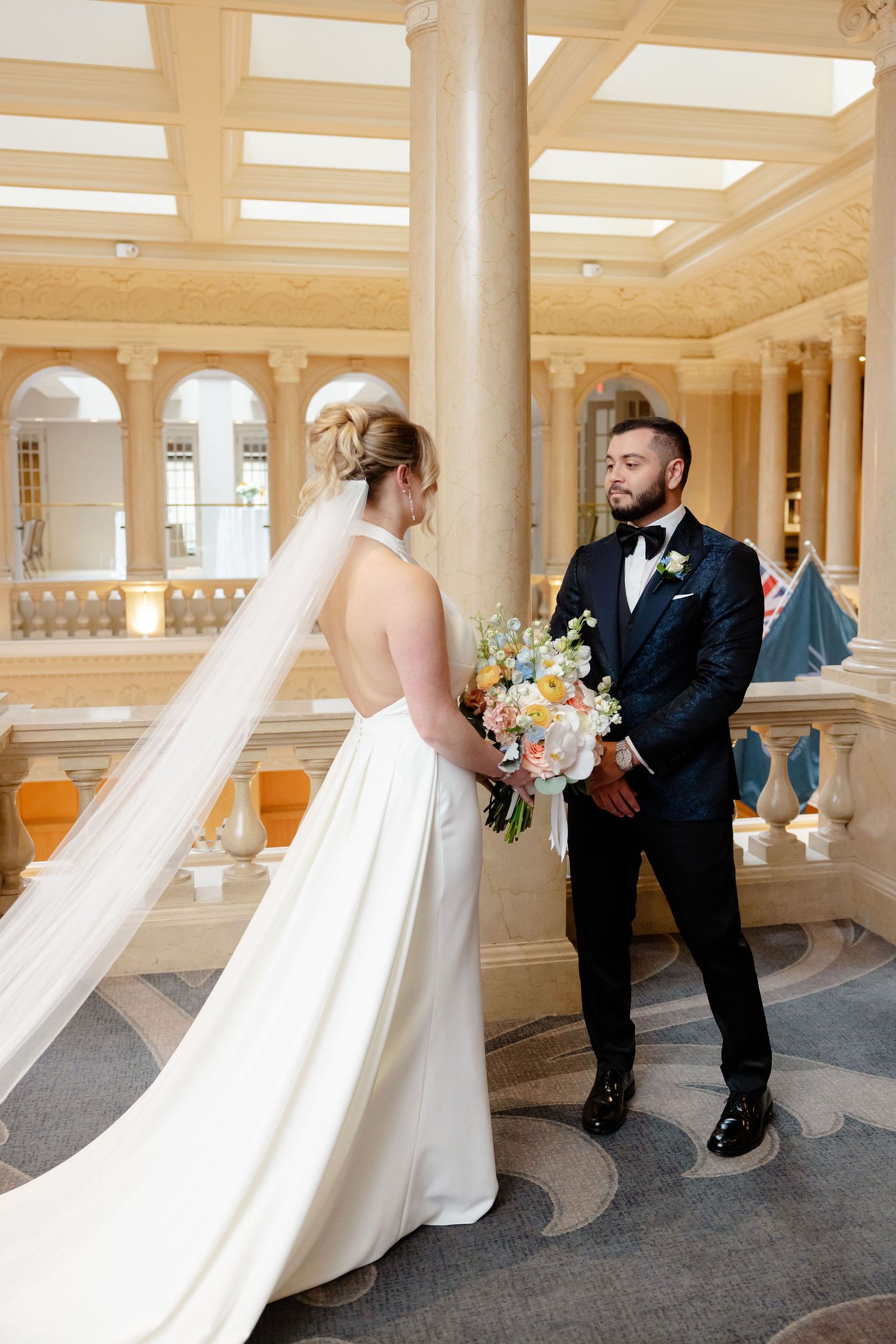 Wedding couple in formal attire sharing a playful moment in an elegant columned hallway.