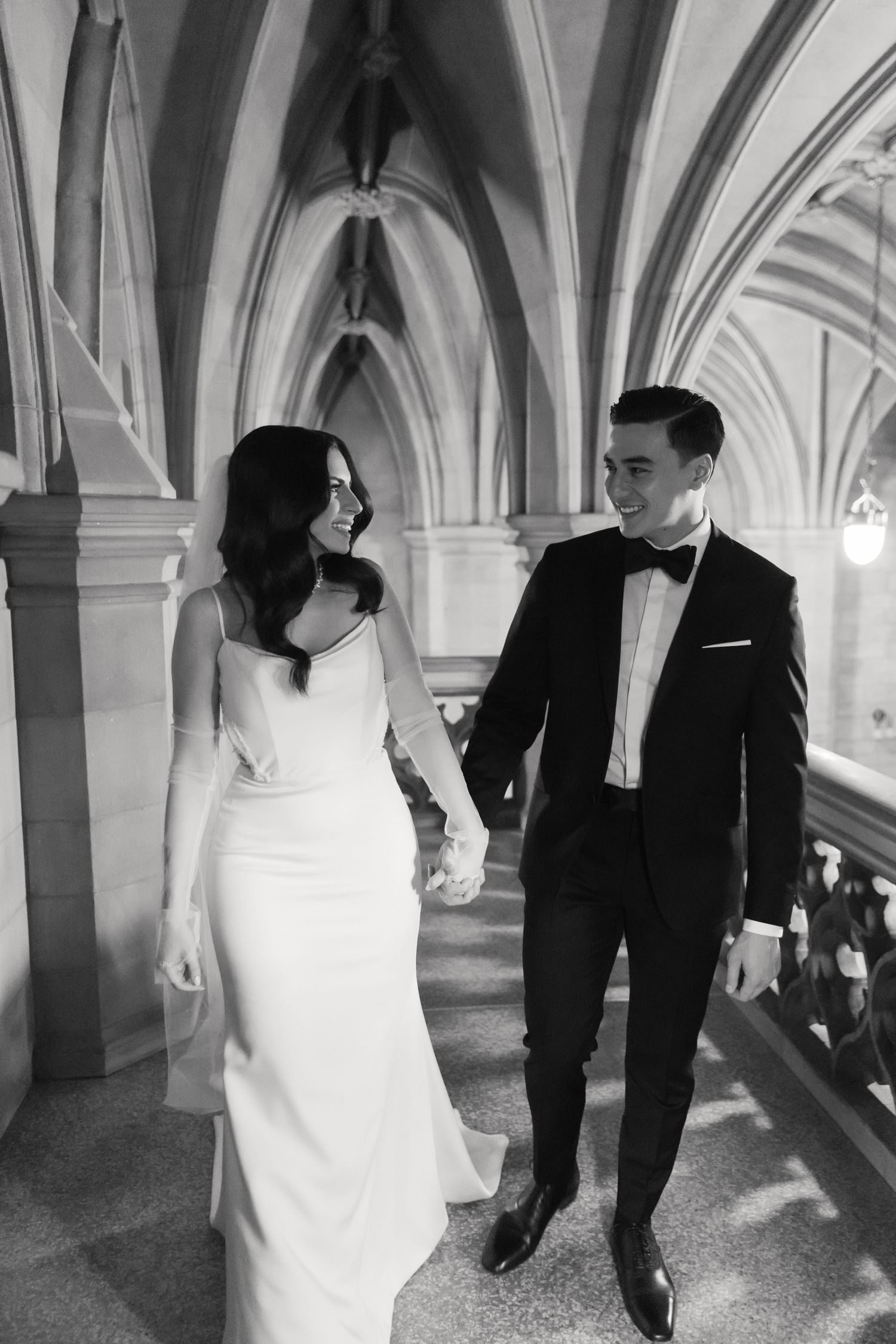 Elegant black and white wedding photo in a gothic corridor with dramatic vaulted ceilings.
