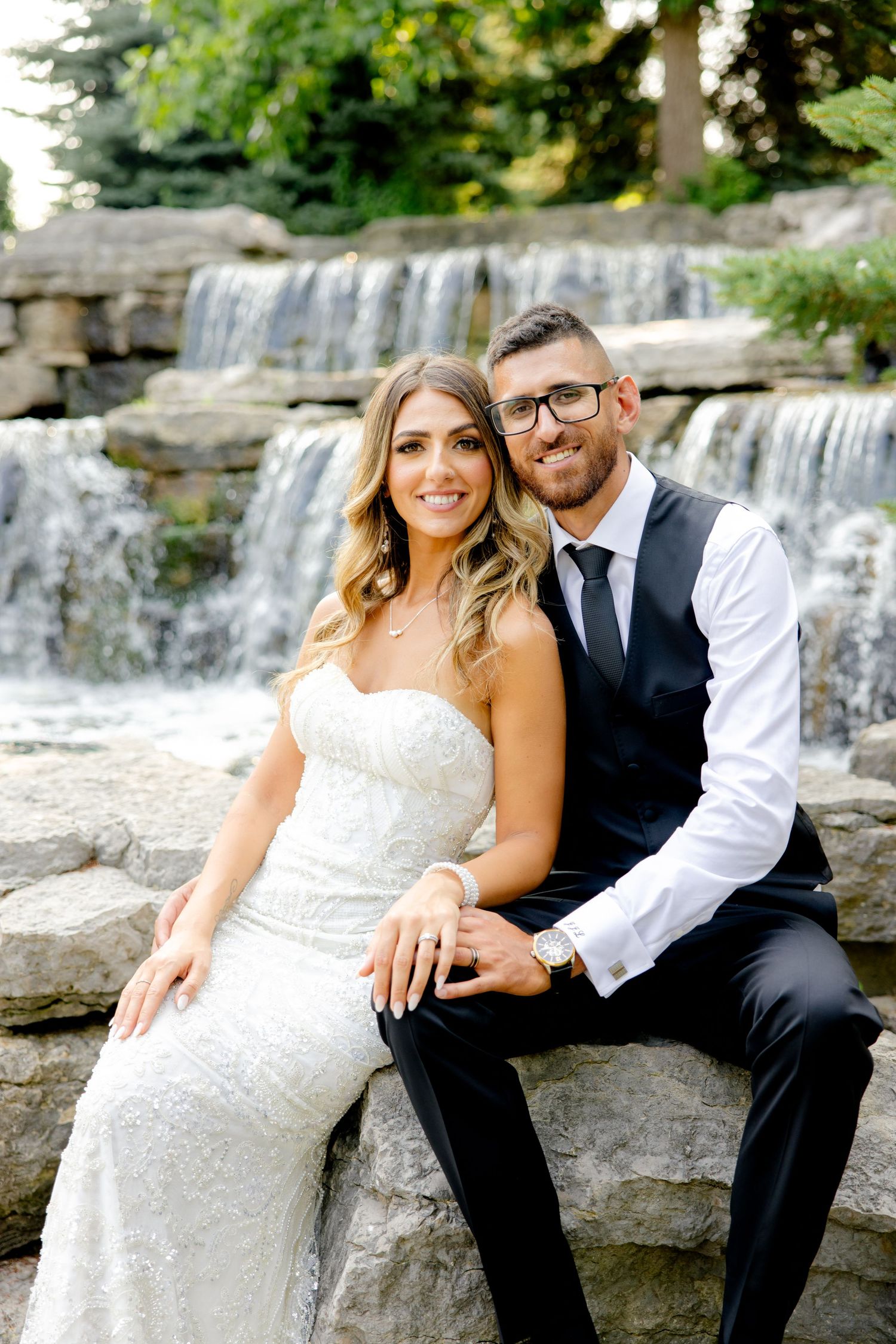 Happy couple poses on stone steps with cascading waterfall behind them.