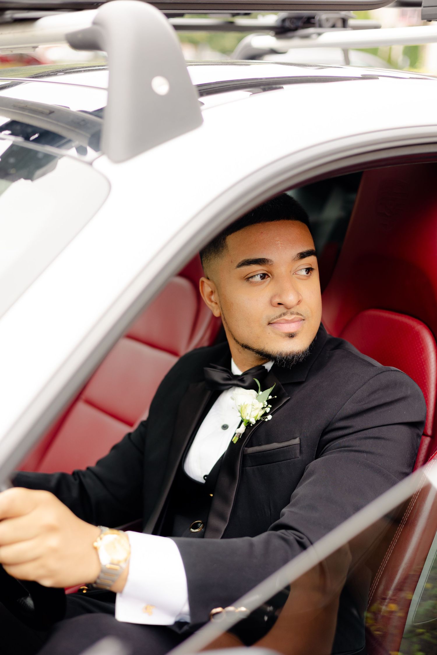 Person in formal attire poses in white luxury car with red interior.