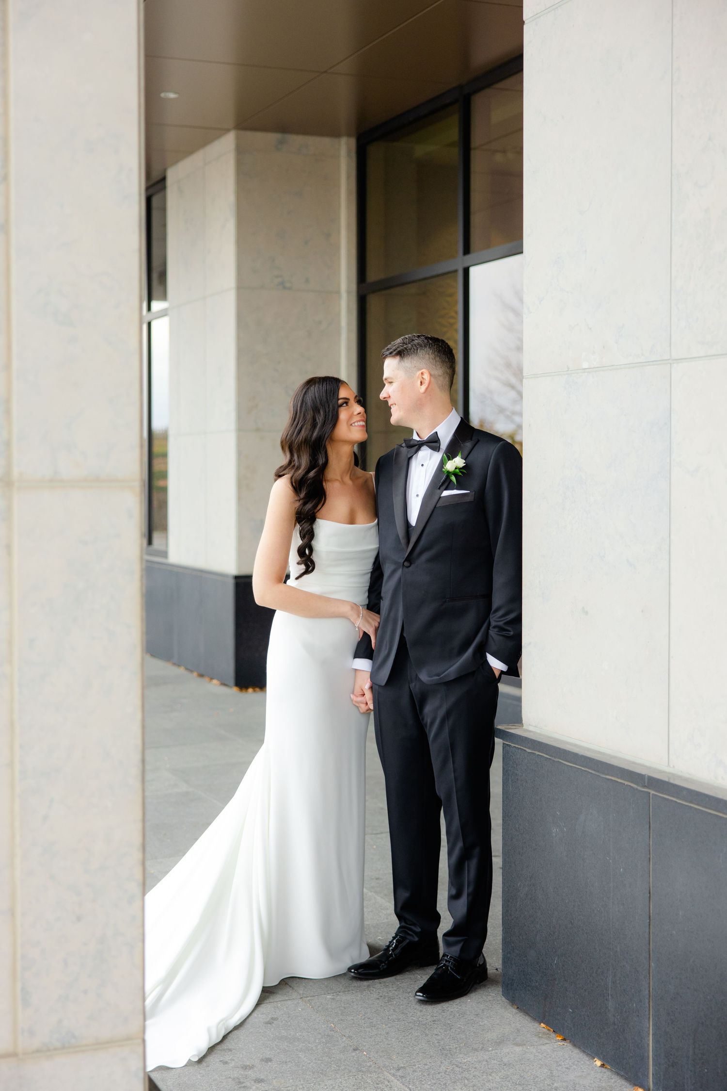 An elegant wedding couple shares a tender moment in front of a modern building exterior.