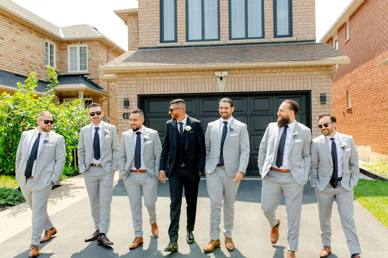 Wedding party in coordinated grey and black attire posing in front of modern brick house.