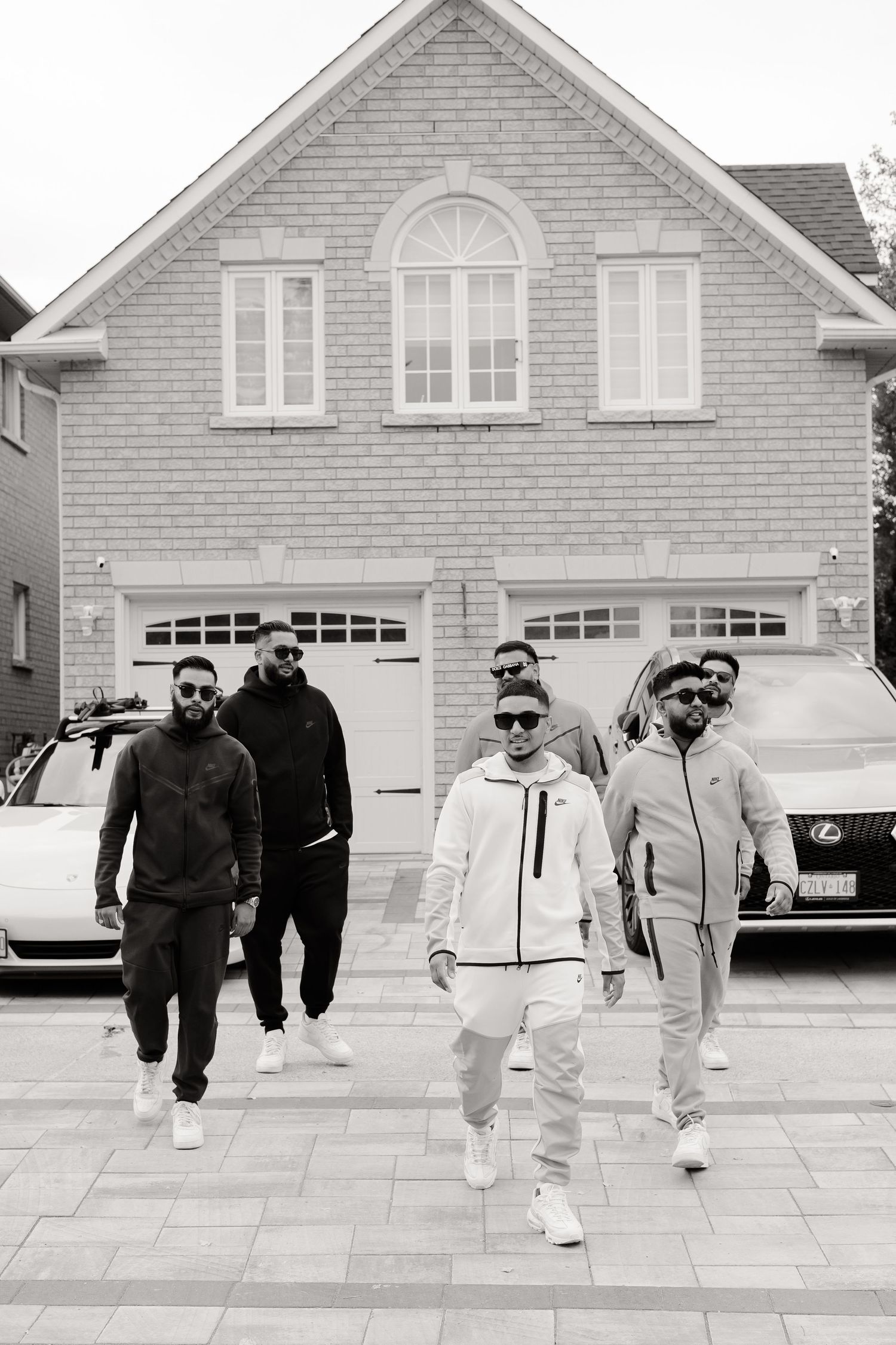 Black and white photo of friends in streetwear walking together in front of a suburban house.