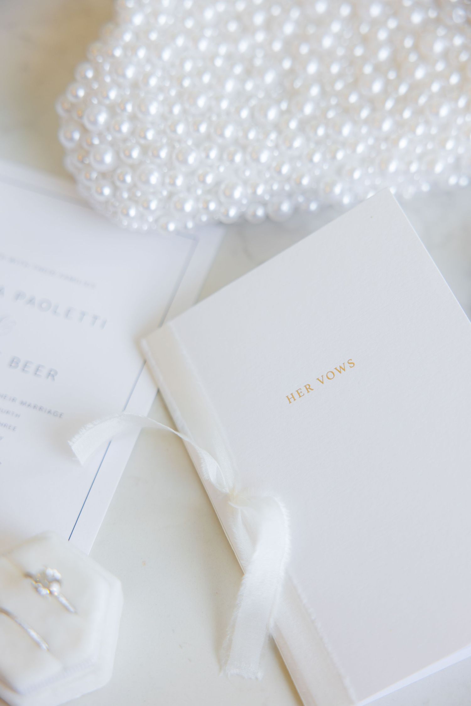 White wedding stationery with pearl clutch and vow book.