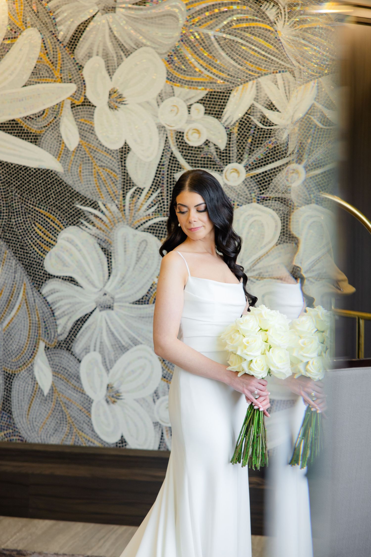 Elegant side profile of a bride in white holding cream flowers against a metallic floral wallpaper.