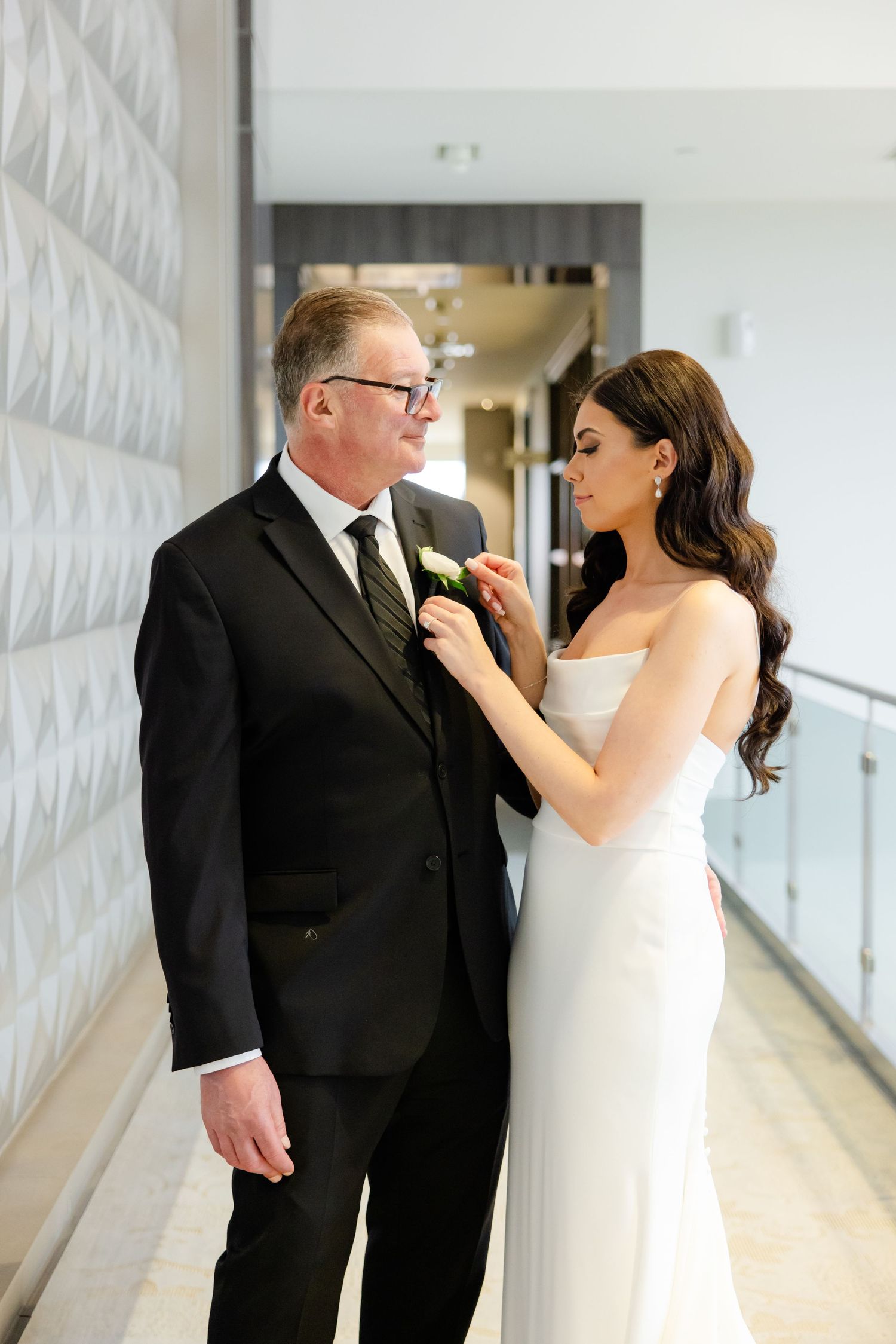 A bride pins a yellow boutonniere onto a black suit jacket.