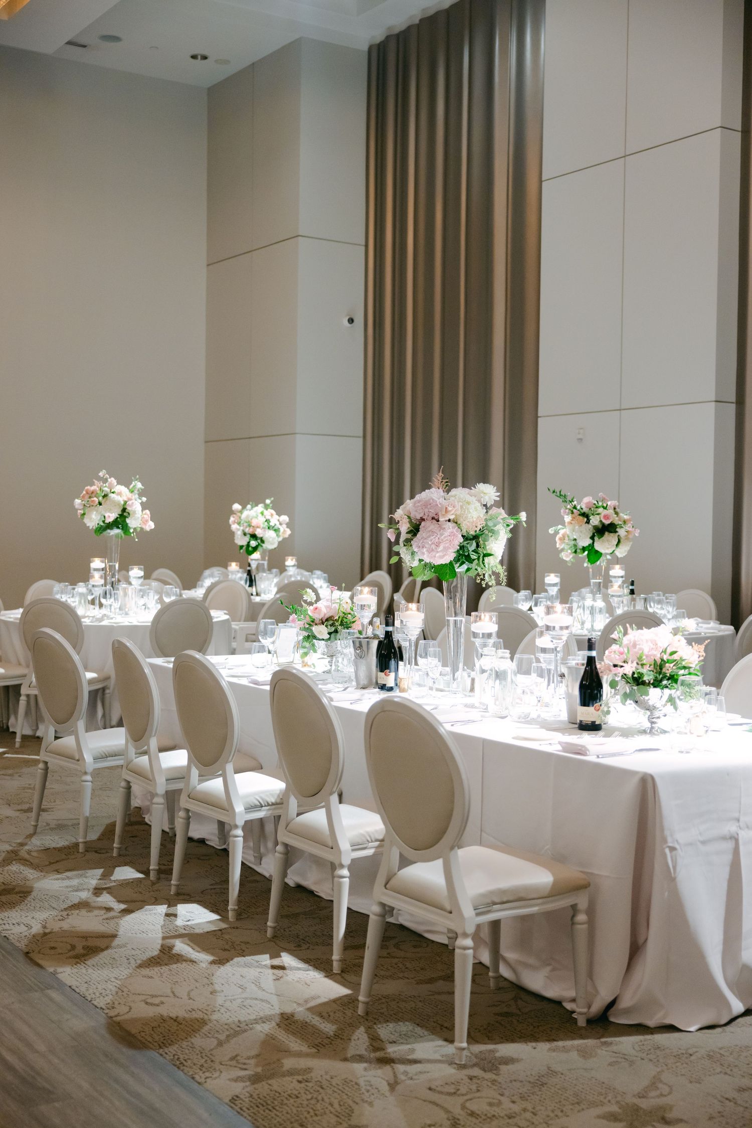 Elegant reception table with white chairs and pink floral arrangements in modern venue.