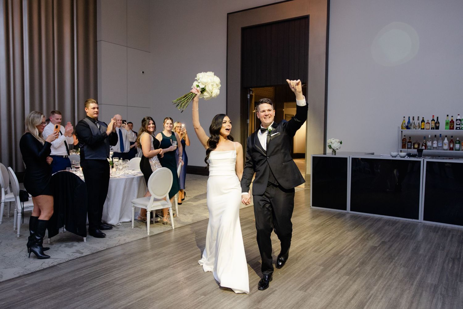 Couple celebrates with raised arms as they make their grand entrance into wedding reception.