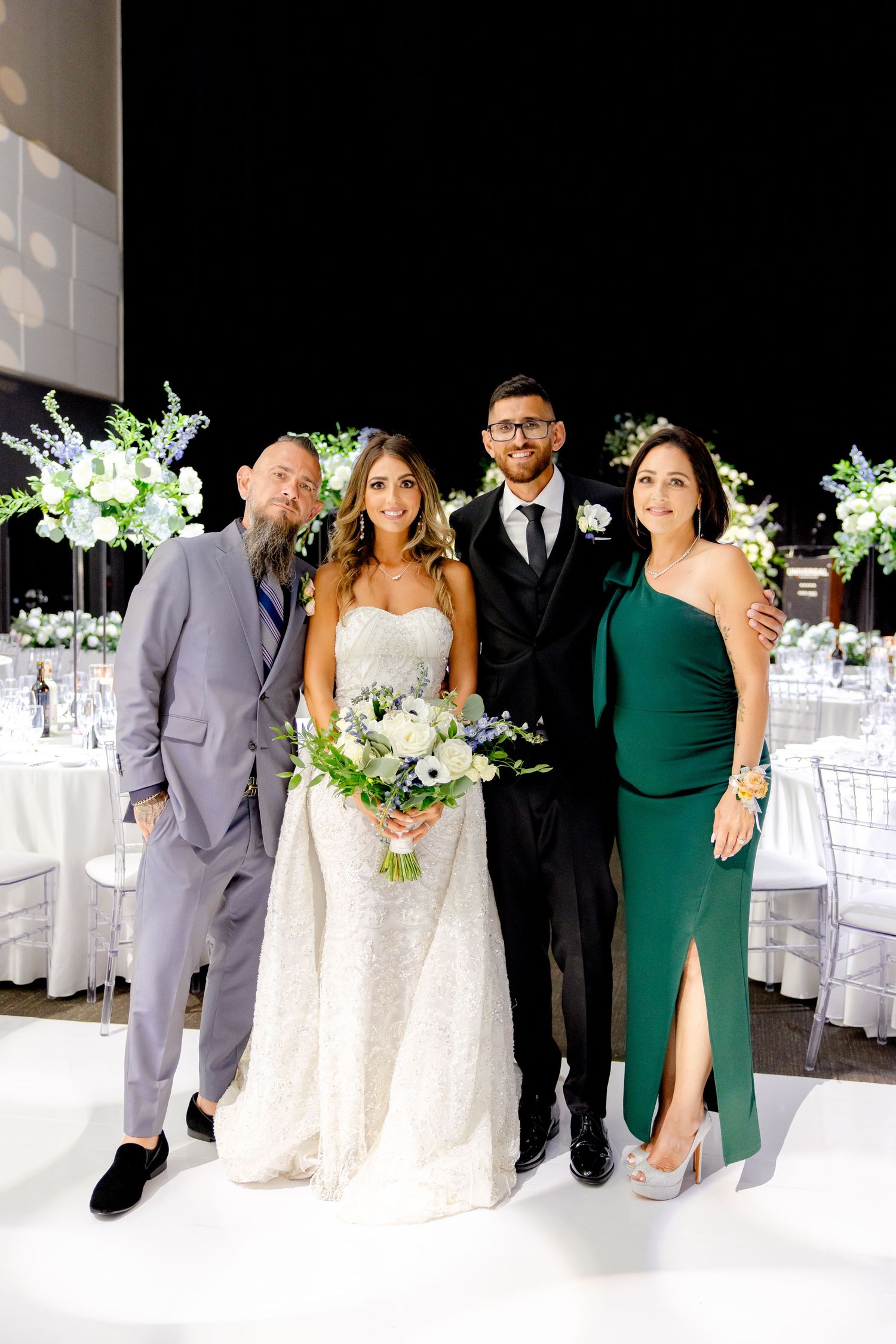 Wedding group photo with bride in white gown and guests in elegant gray and green formal wear.