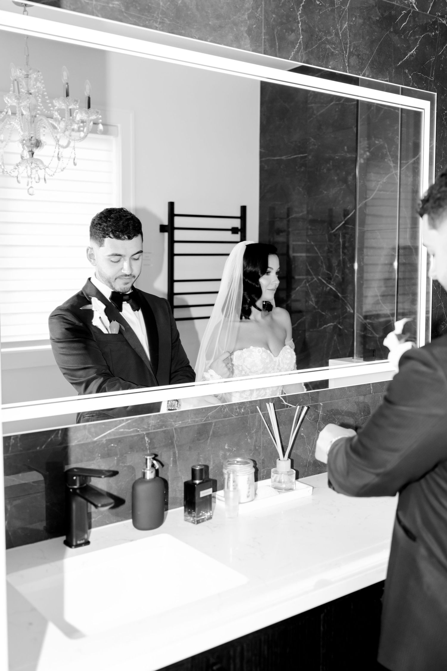 Modern bathroom mirror reflects elegant wedding couple with black marble accent wall.