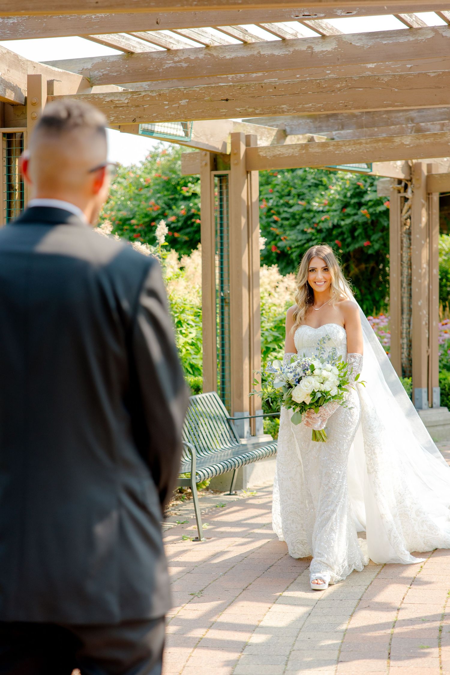 First look wedding moment under wooden pergola with garden backdrop.