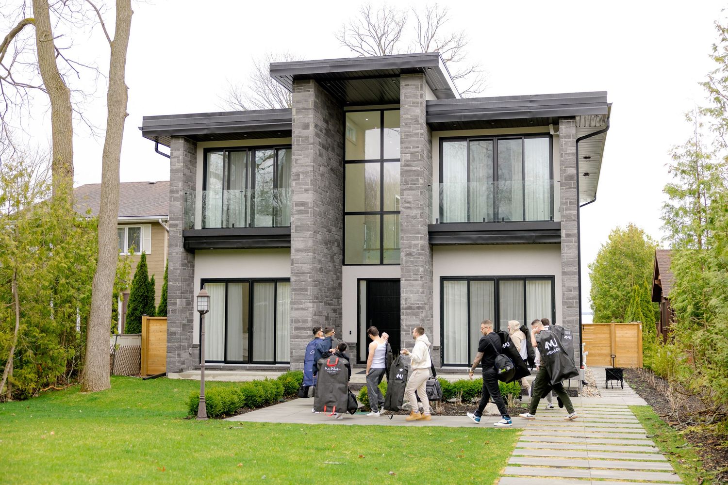 Contemporary grey stone house with large windows and group gathered outside.