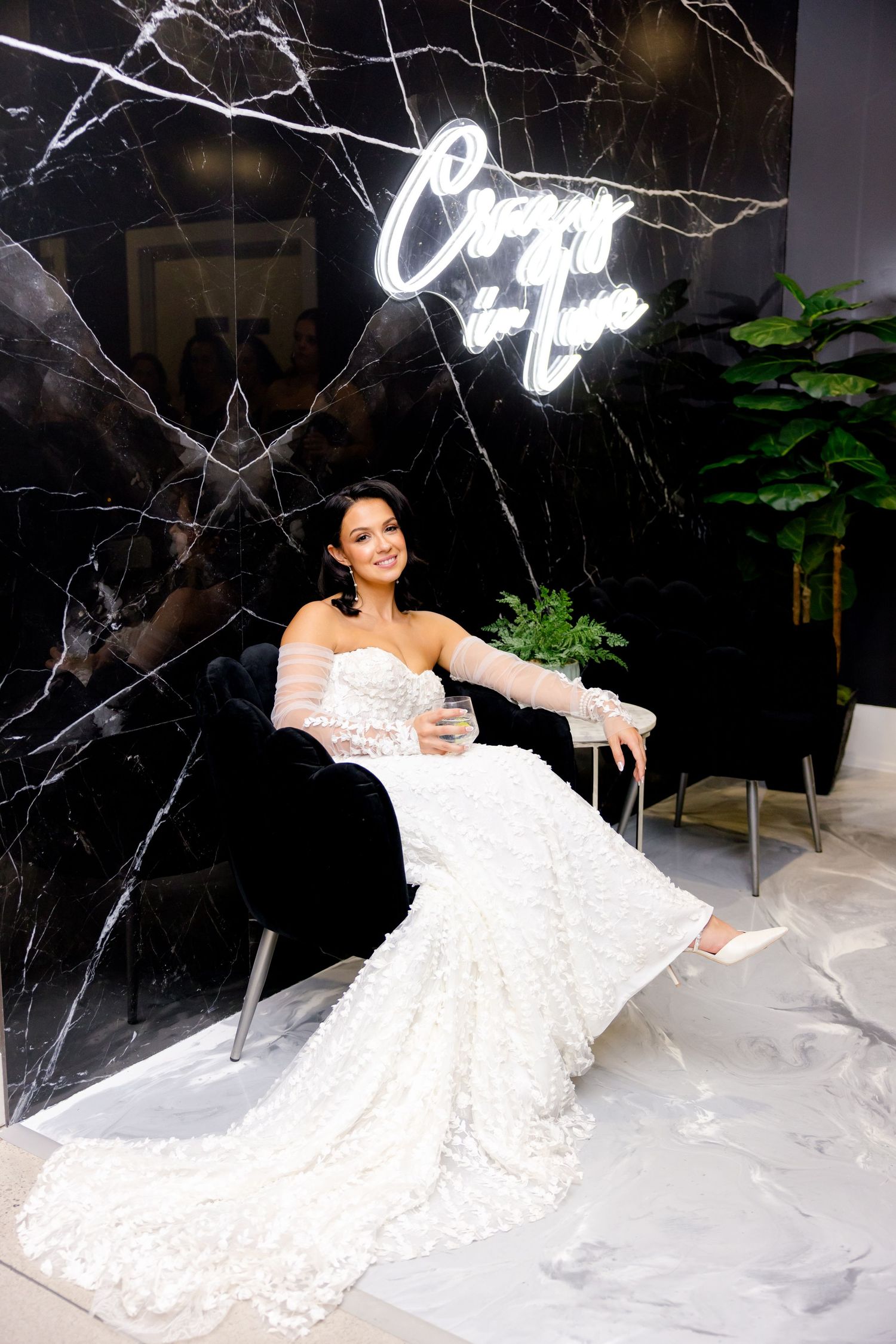 Bride in lace mermaid gown poses against black marble wall with neon sign.