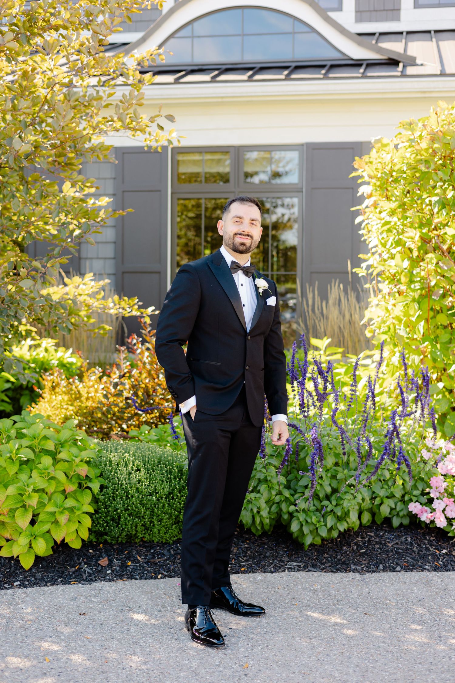 Wedding attire portrait in front of elegant house with autumn foliage and landscaped garden.