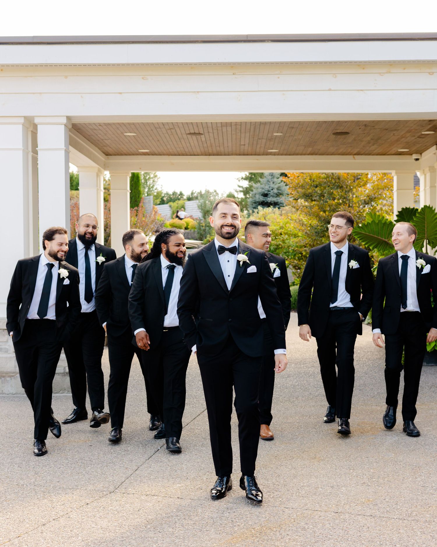 Wedding party in black tuxedos having fun while walking together outdoors.