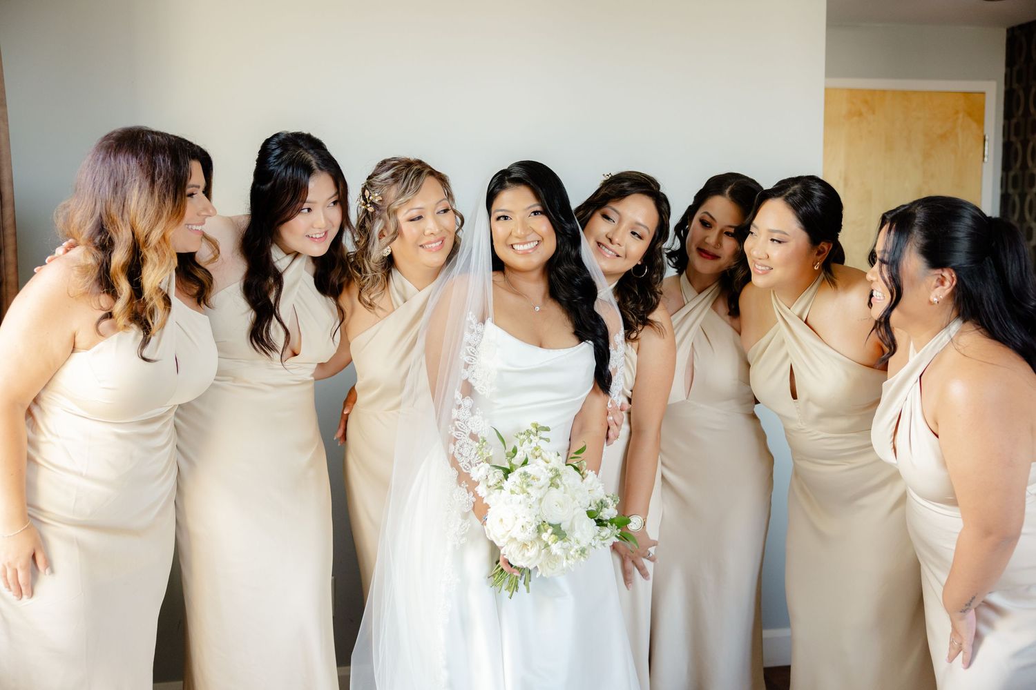 Wedding party shares a candid moment while posing together in matching neutral dresses.